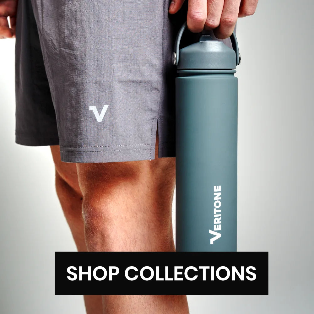 A person in dark gray athletic shorts holds a matte dark gray Veritone water bottle with a carry loop against a plain light gray background. A black banner at the bottom reads 'SHOP COLLECTIONS'.