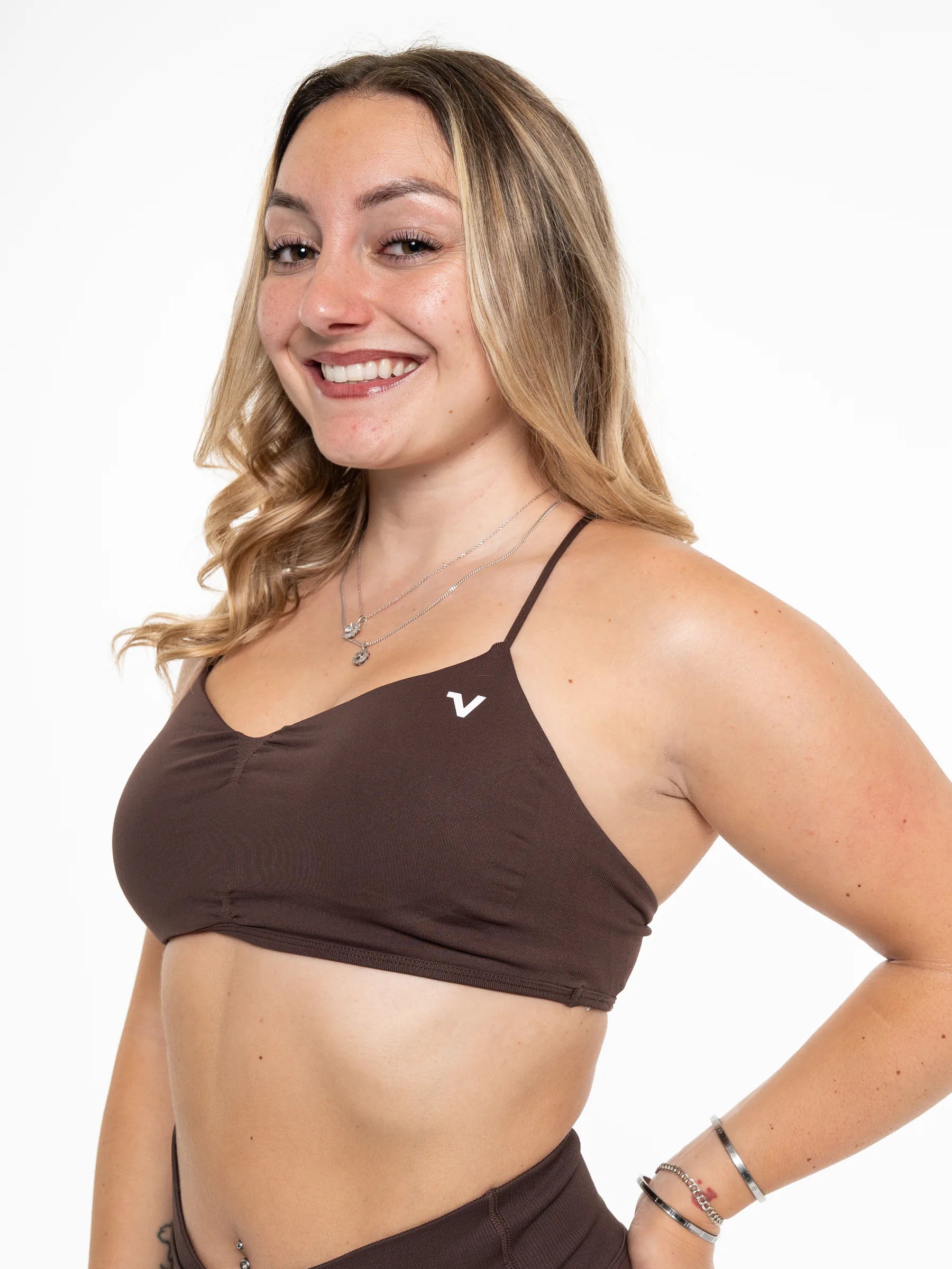 Veritone Ease Bra, Mocha Brown – A smiling woman with blonde-highlighted hair wearing a dark brown ribbed sports bra with a small white stylized 'V' logo on the chest, paired with matching dark brown bottoms, against a plain white background.