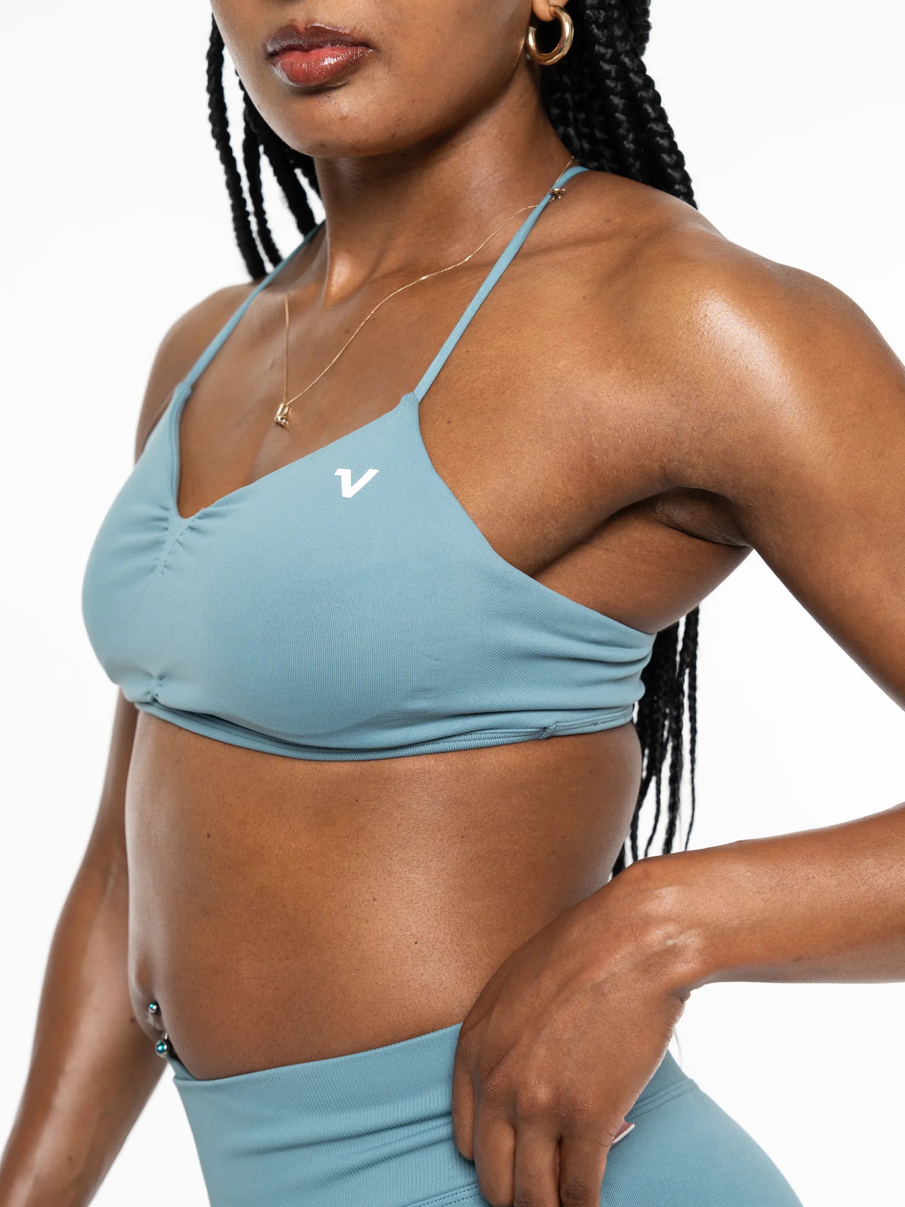 Veritone Ease Bra, Ocean Mist – A close-up of a woman wearing a light blue athletic sports bra with a small white logo on the chest, paired with matching high-waisted bottoms against a plain white background.