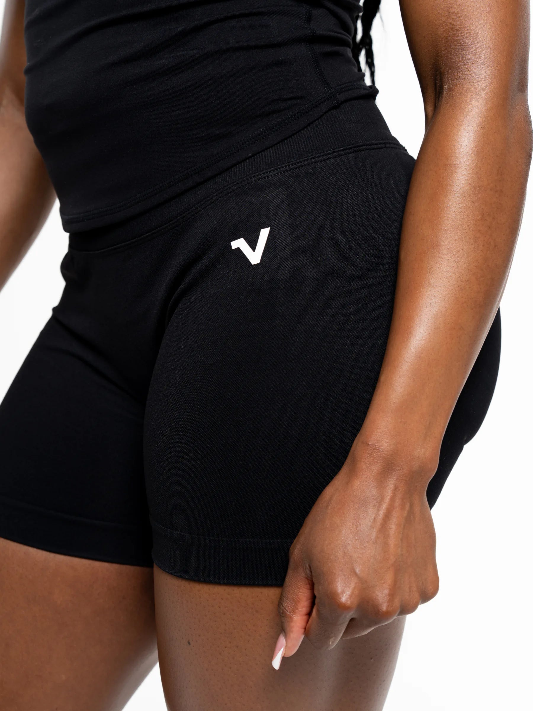 Veritone Ease Shorts, Midnight Black – Close-up of a model wearing black athletic shorts with a small white stylized logo on the left hip, paired with a black top against a plain white background.