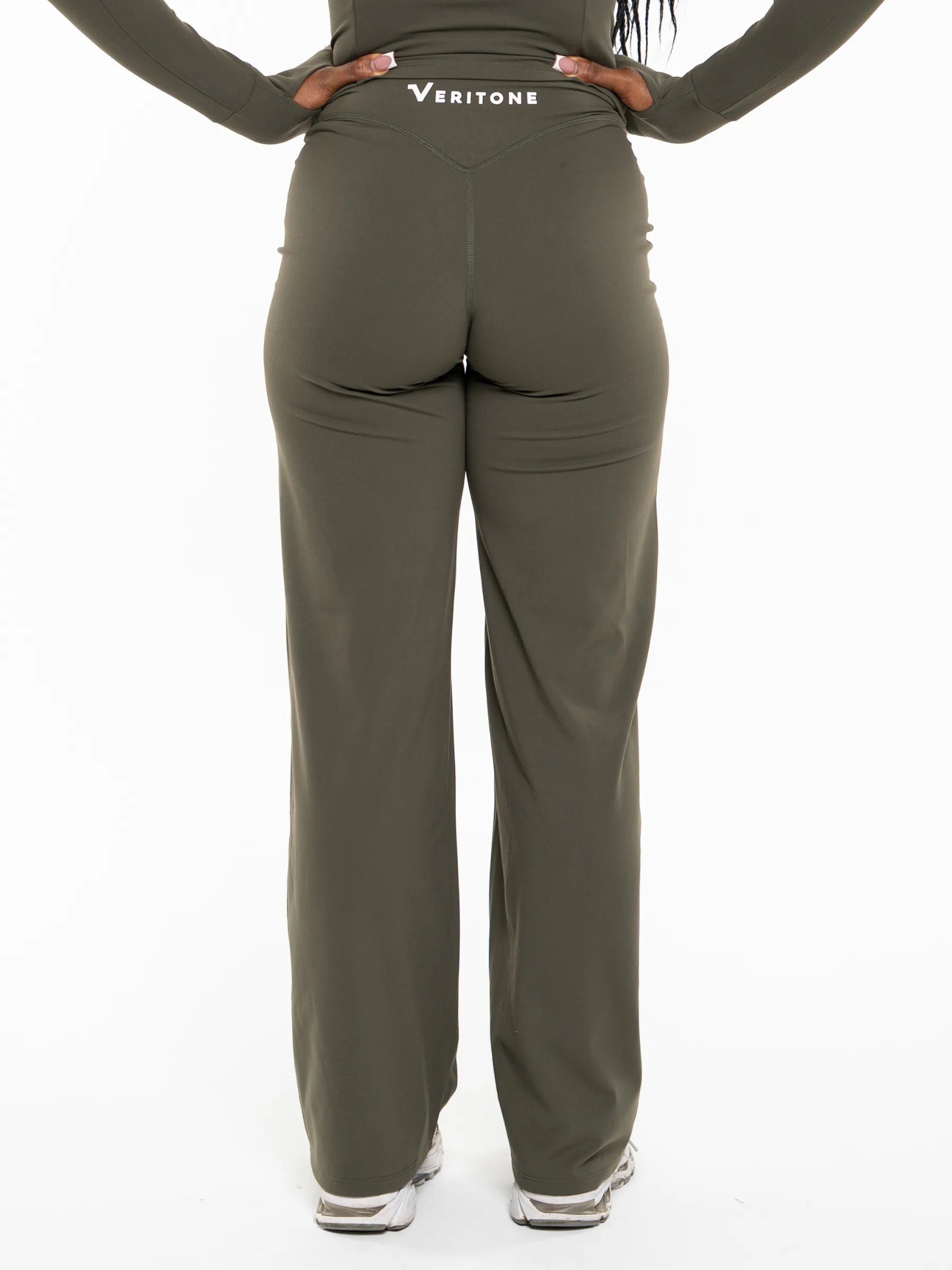 Veritone Élan Flared Pants, Olive Stone – Rear view of a person wearing olive green Veritone athletic pants with a white logo on the back waistband, shown against a plain white background.