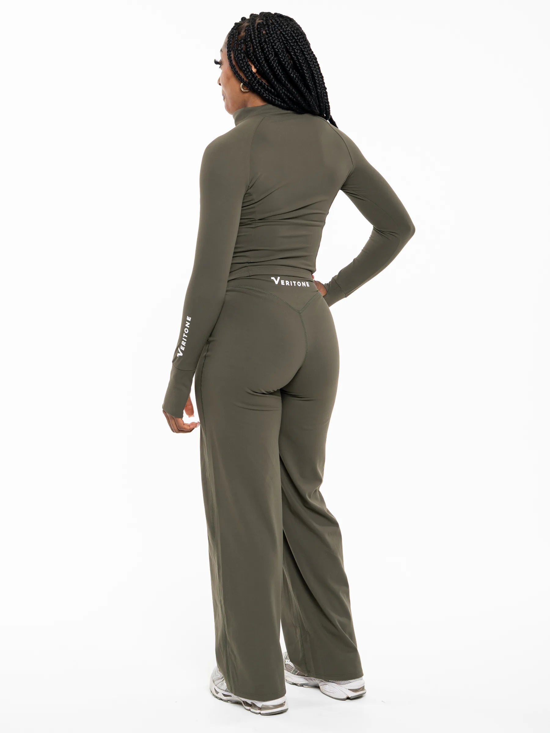 Veritone Élan Flared Pants, Olive Stone – A woman shown from the back wearing a matching olive green long-sleeve track jacket and wide-leg pants set, with white sneakers, against a plain white studio background.