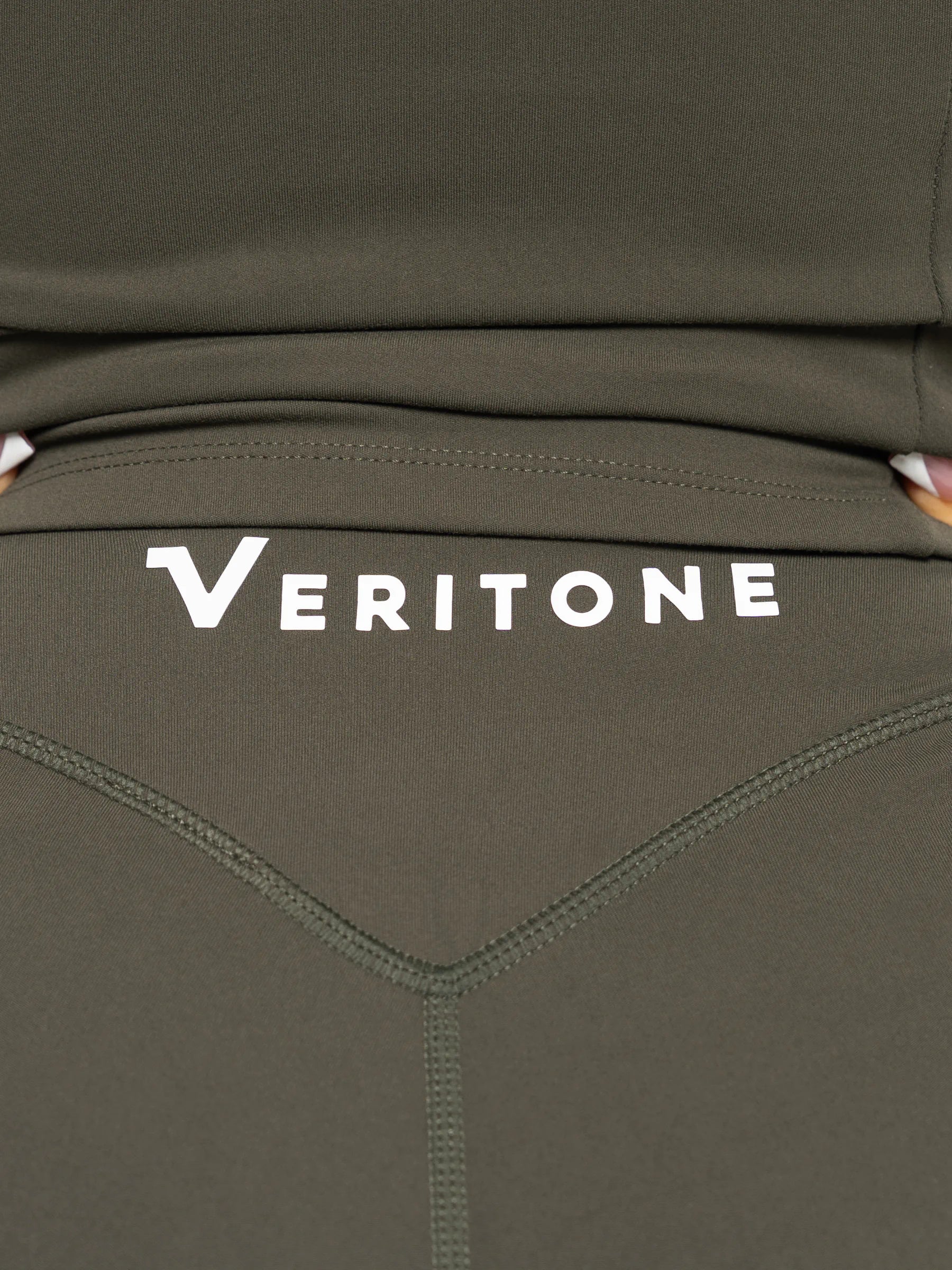 Veritone Élan Flared Pants, Olive Stone – Close-up of olive green athletic leggings with a white 'VERITONE' logo printed across the upper back area.