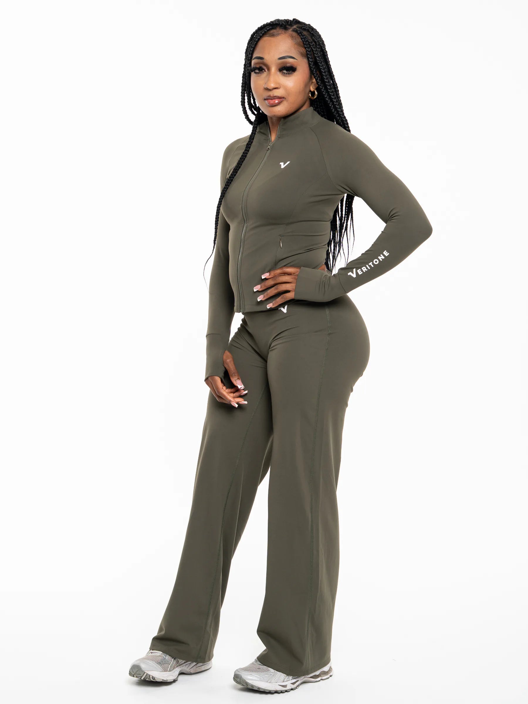 Veritone Élan Flared Pants, Olive Stone – A woman modeling a matching olive green athletic set consisting of a long-sleeve mock-neck zip-up top and wide-leg pants, featuring a small white logo on the chest and sleeve, set against a plain white background.