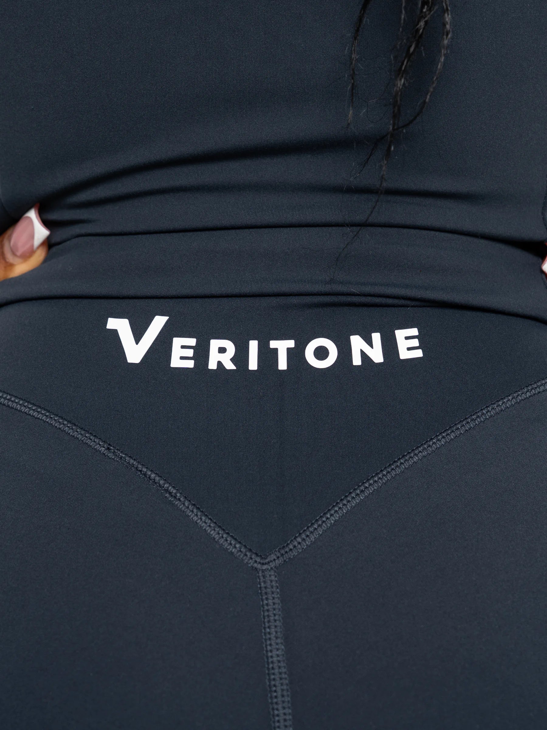 Veritone Élan Flared Pants, Storm Blue – Close-up of a person wearing dark navy leggings with the brand name 'VERITONE' printed in white across the back waistband.
