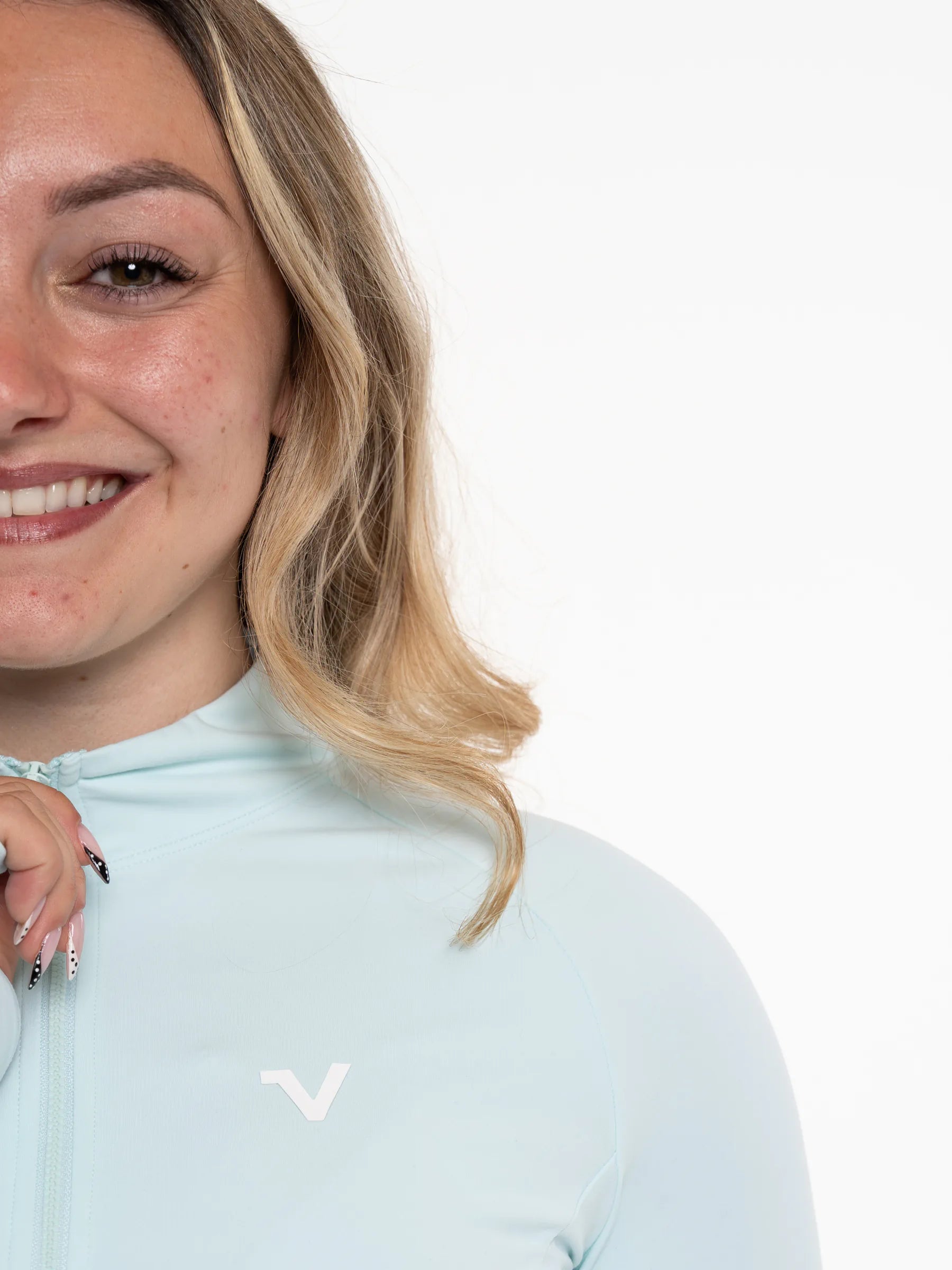 Veritone Élan Jacket, Ocean Mist – Close-up of a smiling woman wearing a light pastel blue high-neck zip-up top with a small white stylized 'V' logo on the chest, against a plain white background.