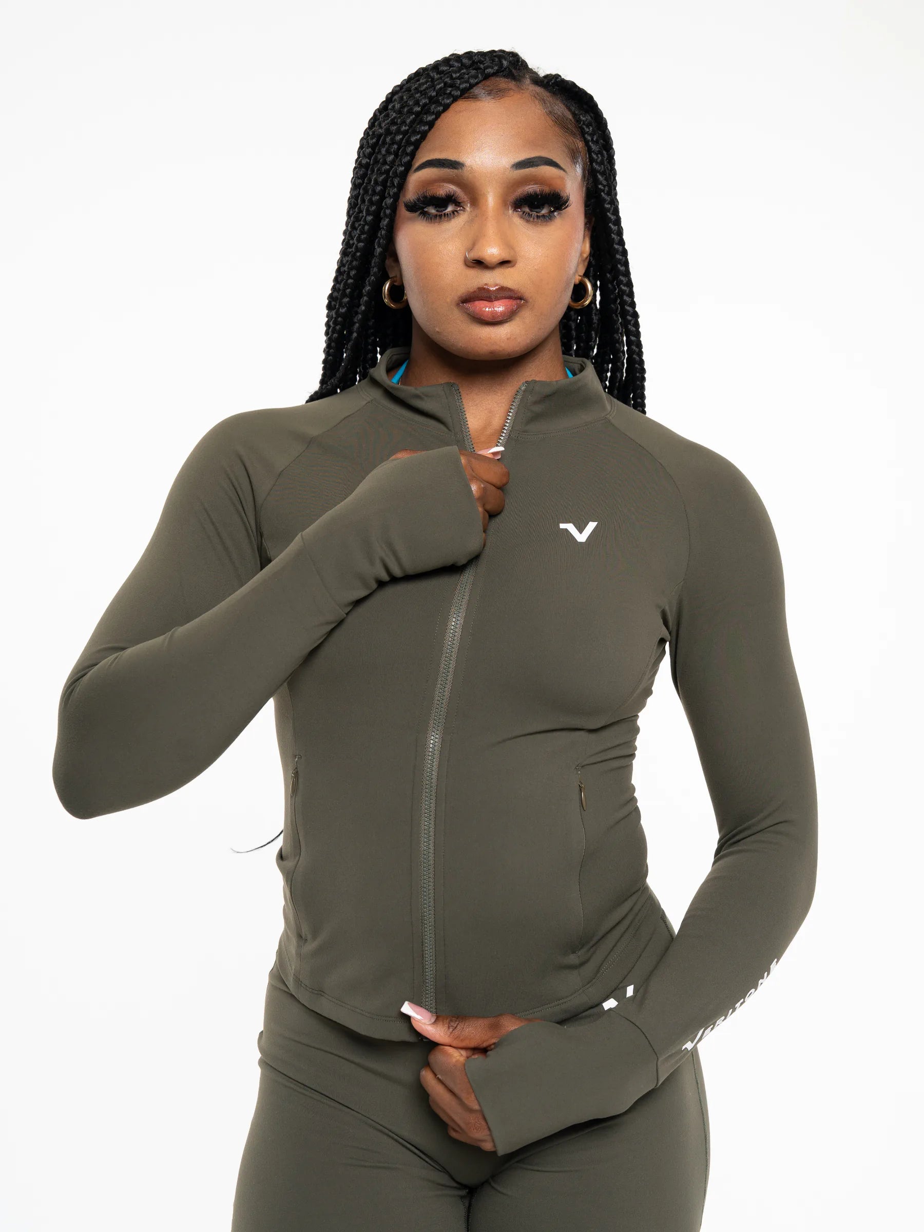Veritone Élan Jacket, Olive Stone – A woman modeling a fitted long-sleeve athletic zip-up jacket in olive green, paired with matching leggings, against a plain white studio background.