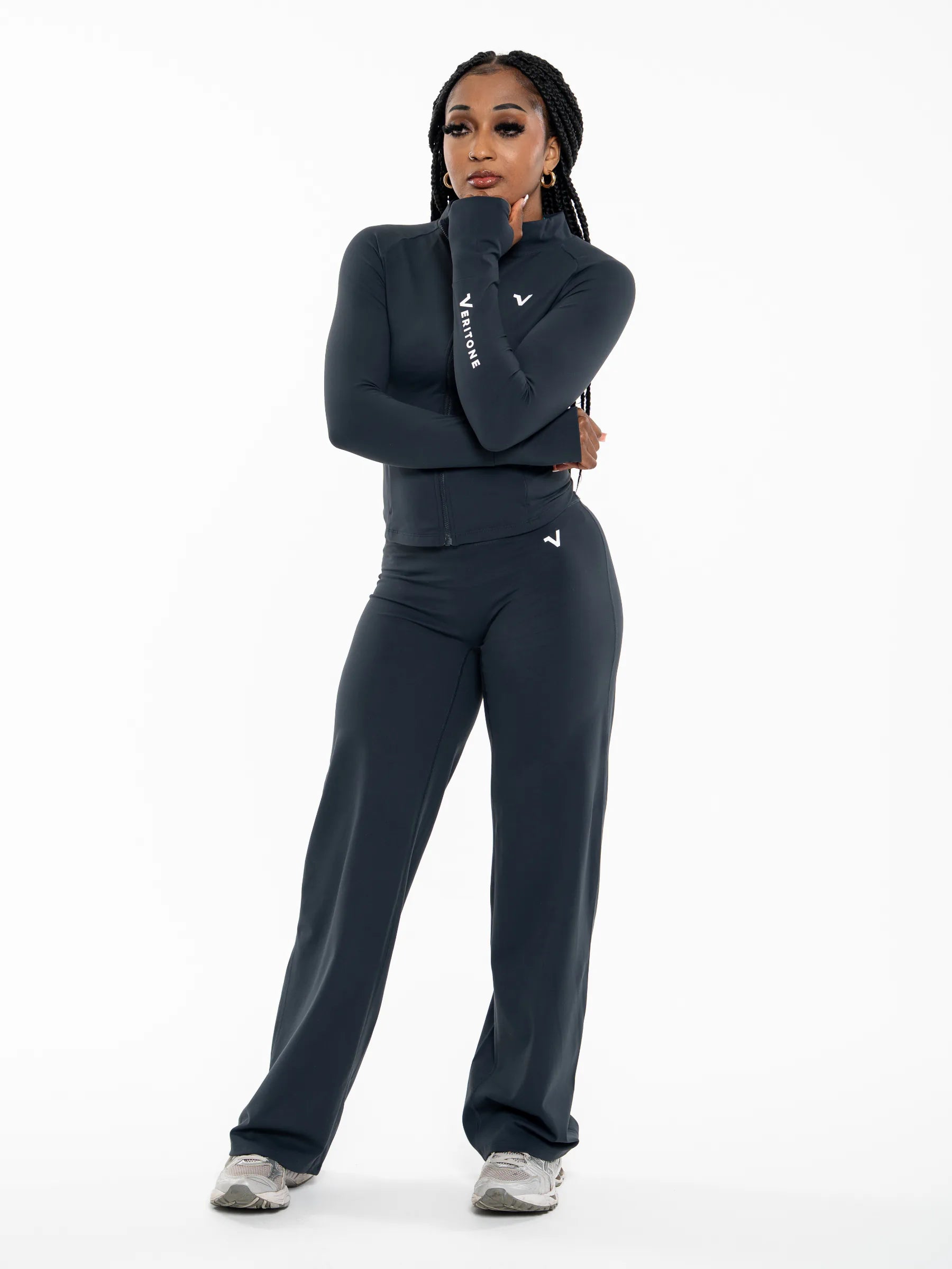Veritone Élan Jacket, Storm Blue – A woman modeling a dark navy athletic set consisting of a long-sleeve zip-up top and matching wide-leg pants, with white Nike logos visible on the chest and sleeve, set against a plain white studio background.