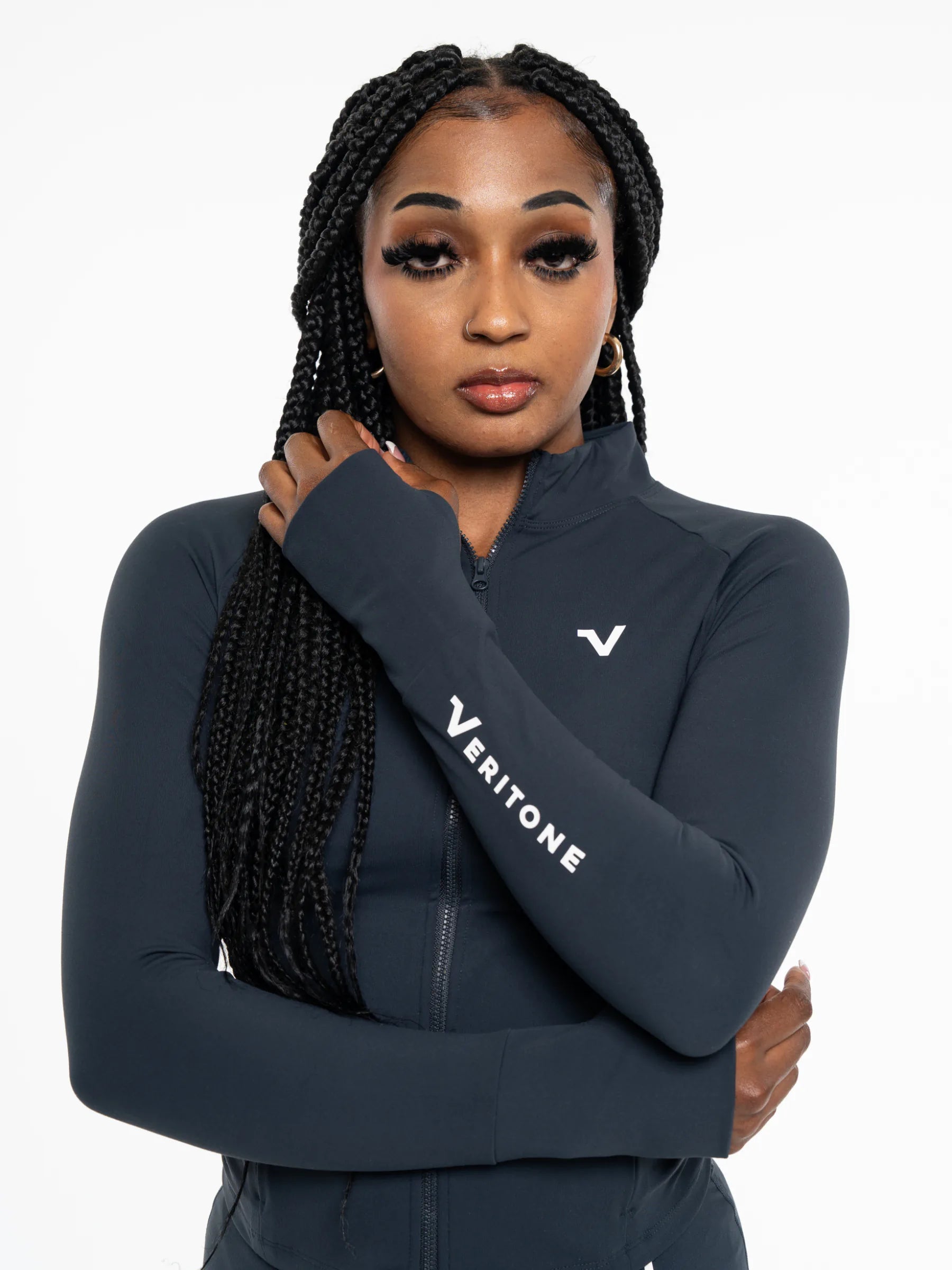 Veritone Élan Jacket, Storm Blue – A woman with black box braids wearing a dark navy Veritone long-sleeve athletic zip-up jacket, posed against a solid white background.