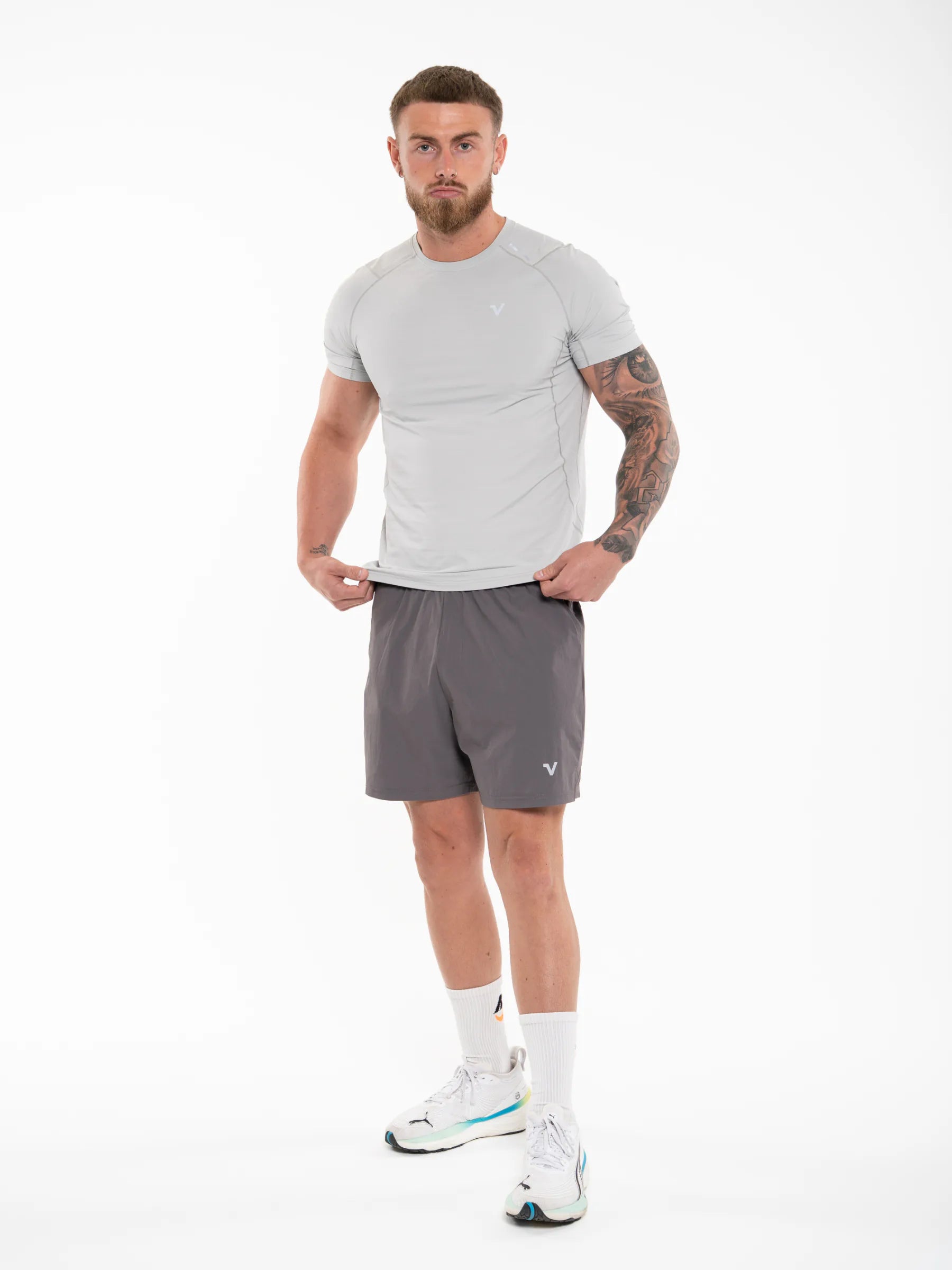 Veritone Essential Training Shorts, Ash Grey – dark gray athletic shorts modeled by a man in athletic wear, featuring a light gray short-sleeve compression shirt and dark gray athletic shorts, standing against a plain white studio background.