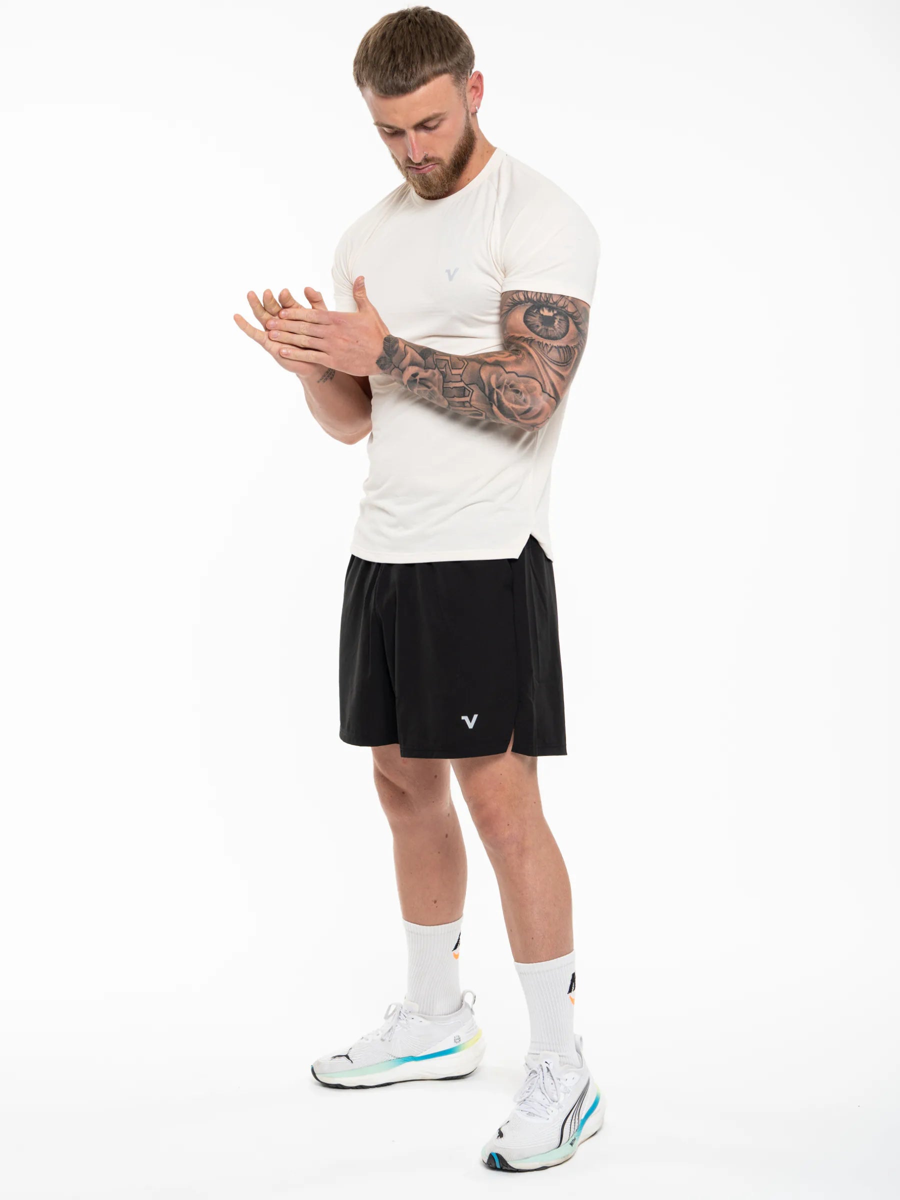 Veritone Essential Training Shorts, Black athletic shorts modelled by a man wearing a white athletic t-shirt, black athletic shorts, white socks, and white sneakers with light blue accents, standing against a white studio background.