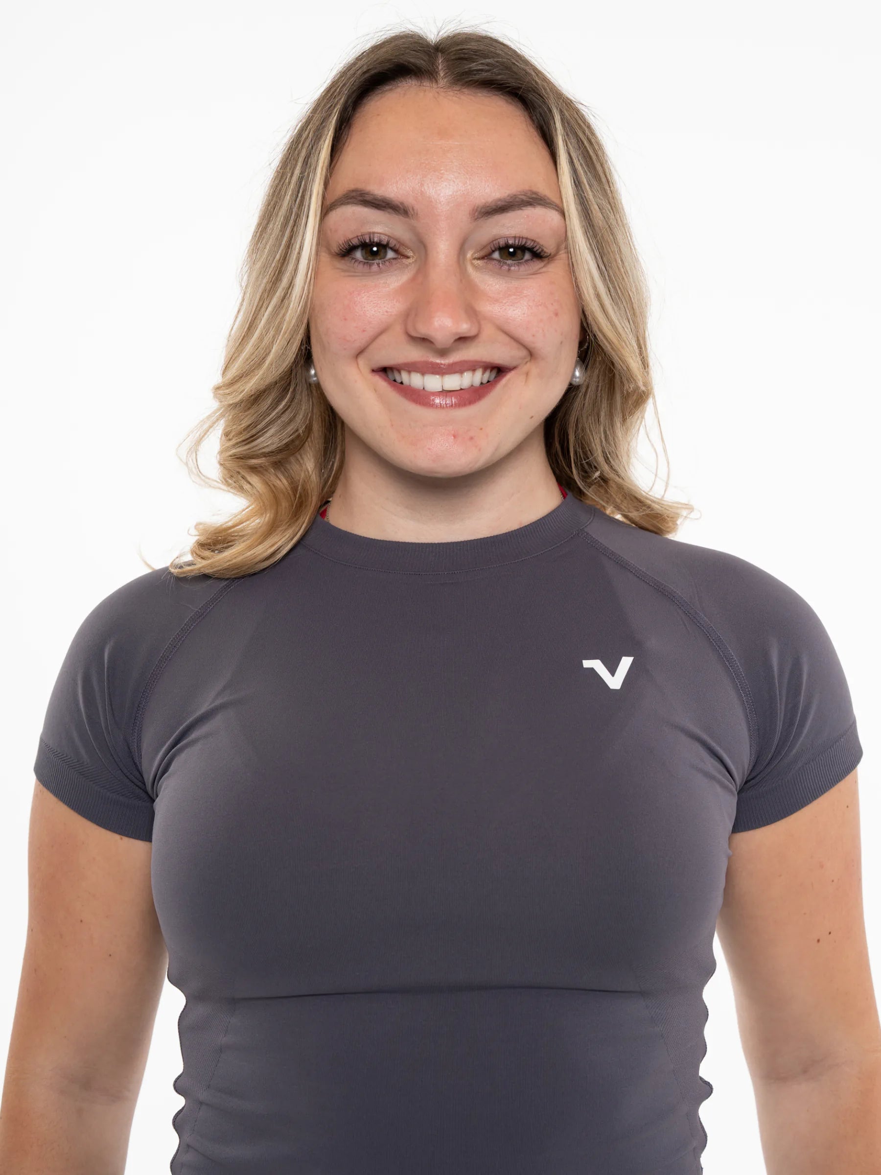 Veritone Form T-Shirt, Graphite Grey – A smiling blonde woman wearing a dark gray short-sleeve athletic top with a small white stylized 'V' logo on the left chest, photographed against a plain white background.