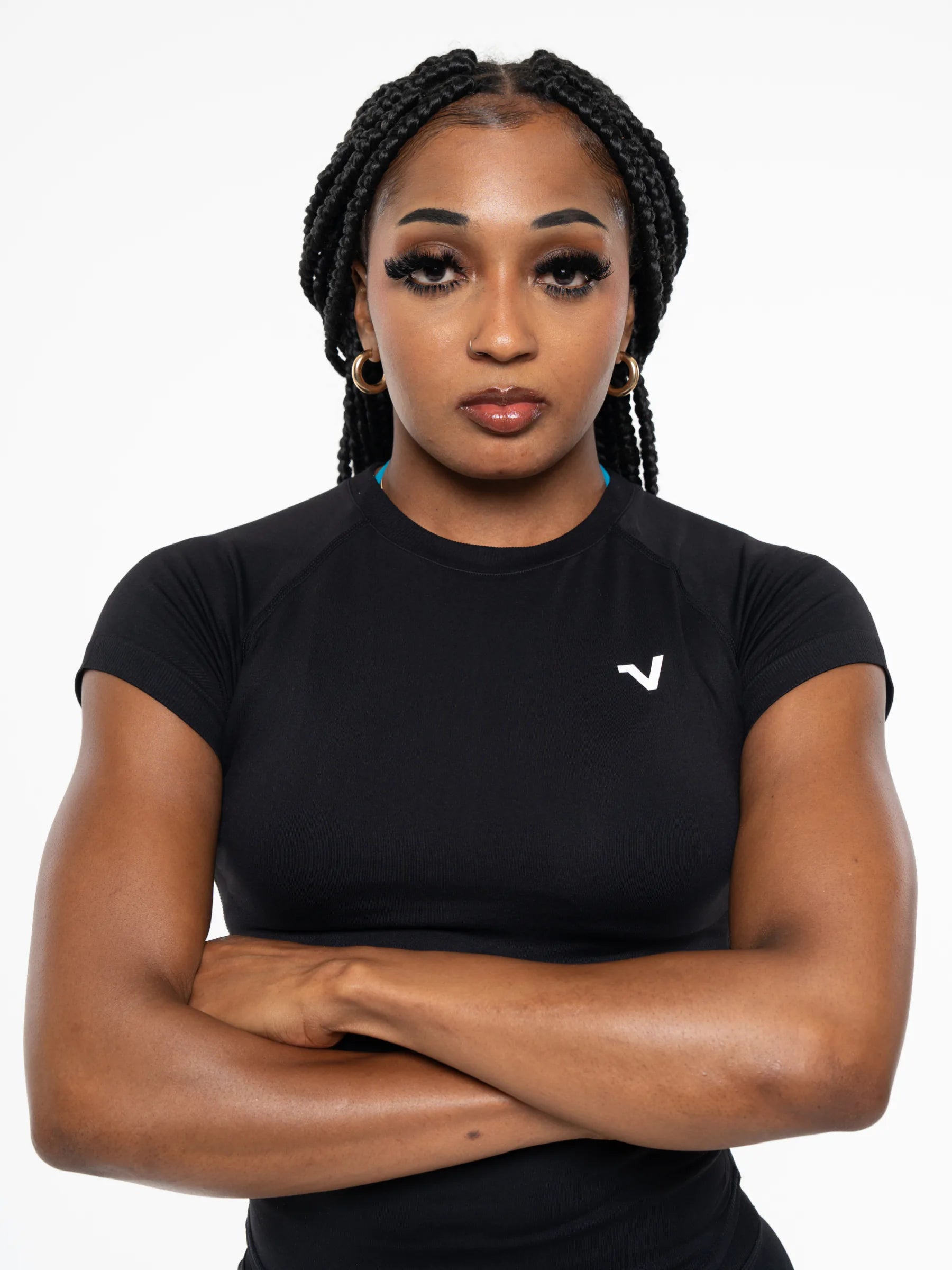 Veritone Form T-Shirt, Midnight Black – A woman with braided hair wearing a fitted black short-sleeve athletic top with a small white logo on the left chest, posed with arms crossed against a plain light gray background.