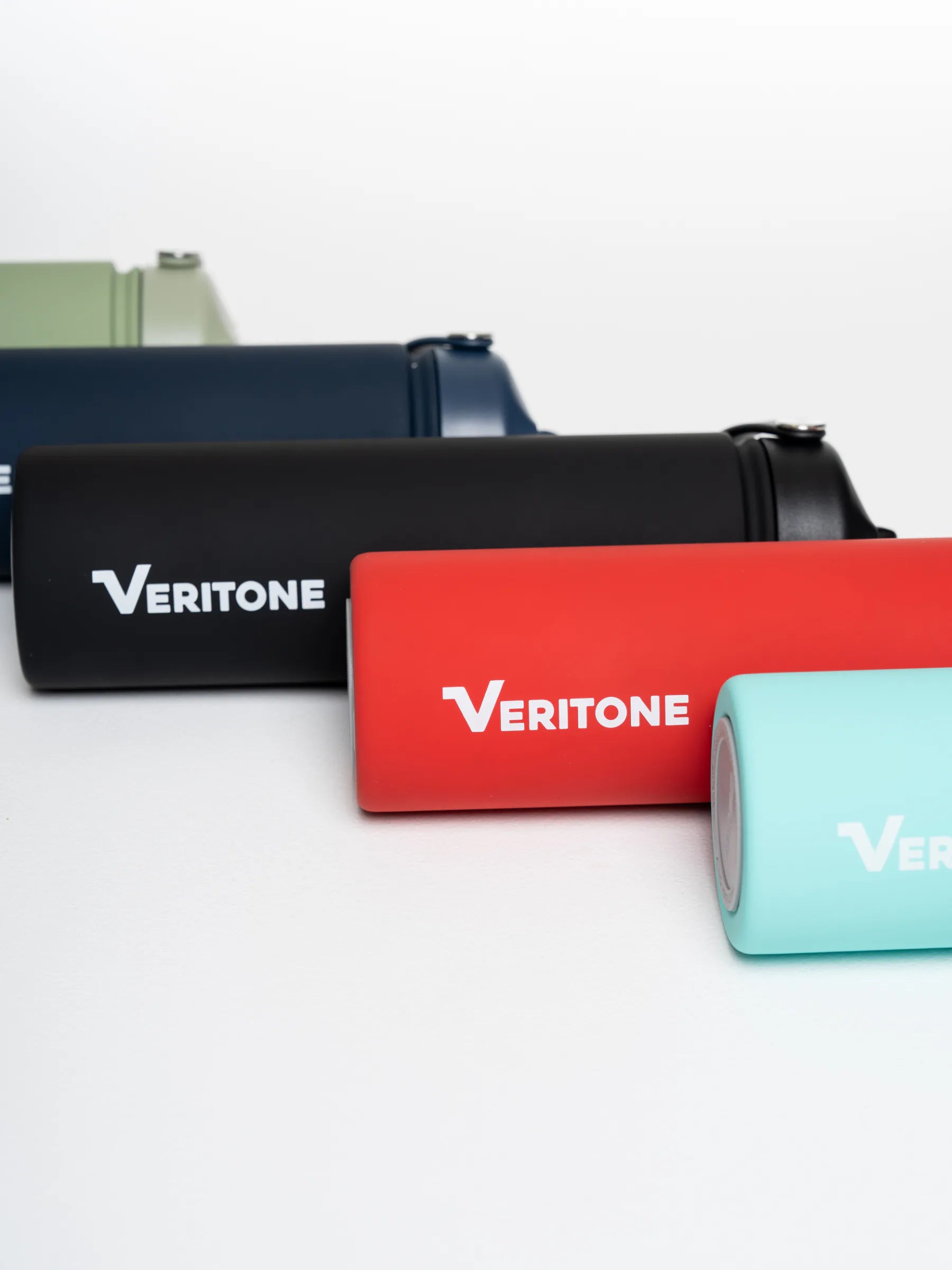 Four cylindrical Veritone hydration bottles in different colors (olive green, navy blue, black, red, and mint green) arranged diagonally on a clean white background.