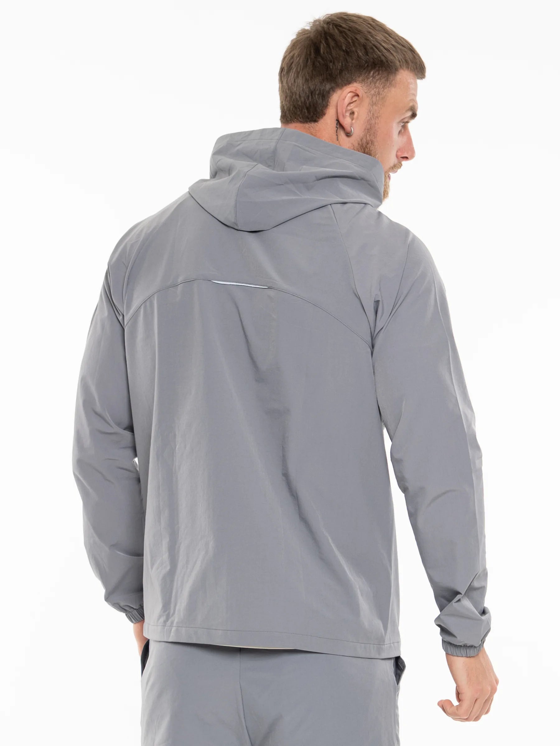Veritone Mode Jacket, Ash Grey – A man wearing a light gray hooded windbreaker jacket, shown from the back and side against a plain white studio background.