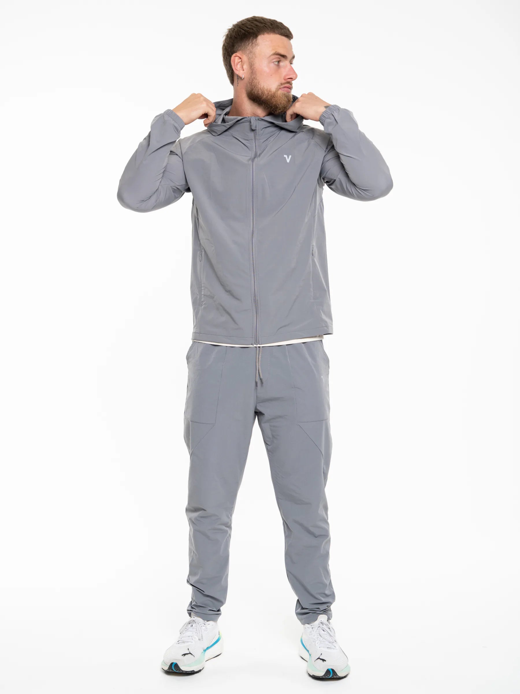 Veritone Mode Jacket, Ash Grey – A man wearing a matching gray athletic tracksuit with a zip-up jacket and jogger pants, posing against a plain white background.