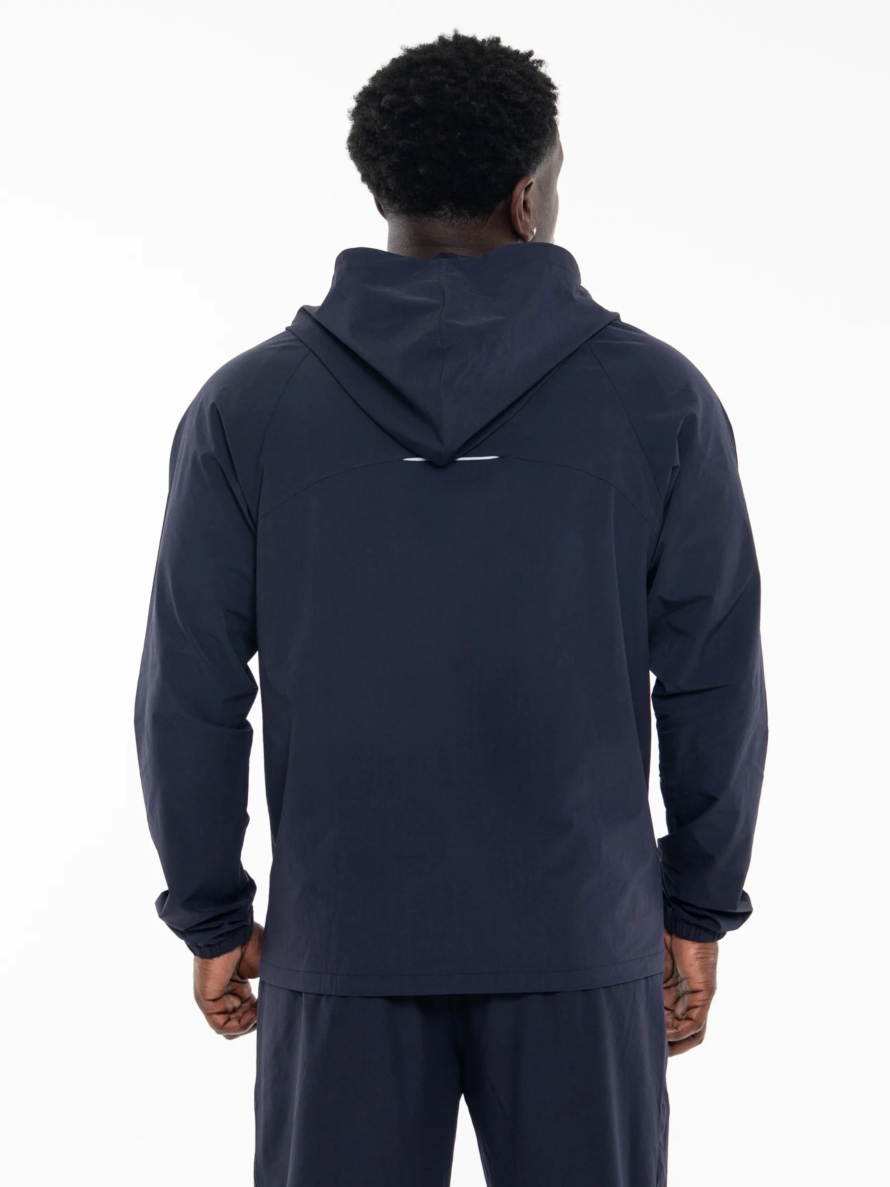 Veritone Mode Jacket, Deep Navy – A man viewed from the back wearing a dark navy hooded sweatshirt and matching navy pants against a plain white studio background.