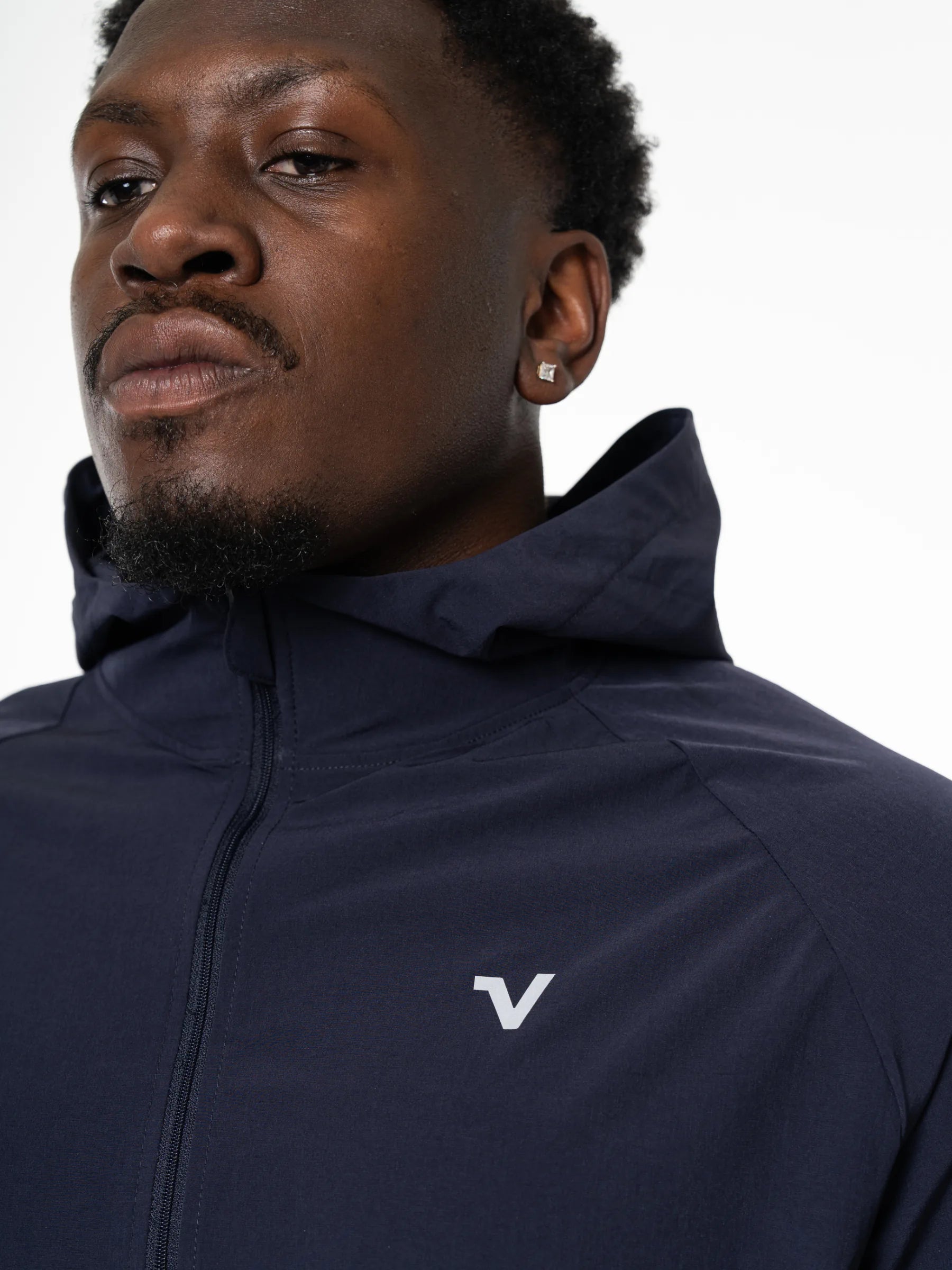 Veritone Mode Jacket, Deep Navy – Close-up of a man wearing a navy blue hooded jacket with a white stylized 'V' logo on the left chest, photographed against a plain light background.