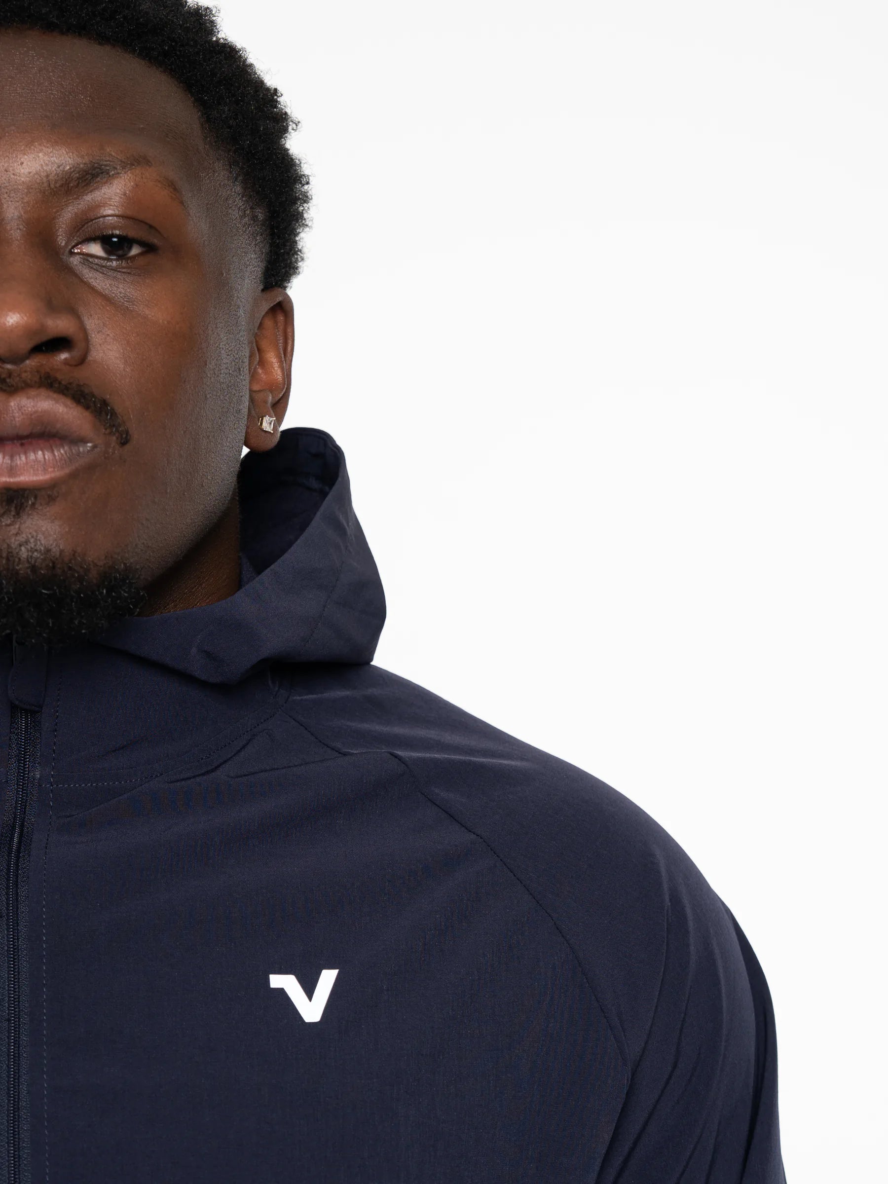 Veritone Mode Jacket, Deep Navy – Close-up of a man wearing a navy hooded jacket with a small white stylized 'V' logo on the chest, against a plain white background.