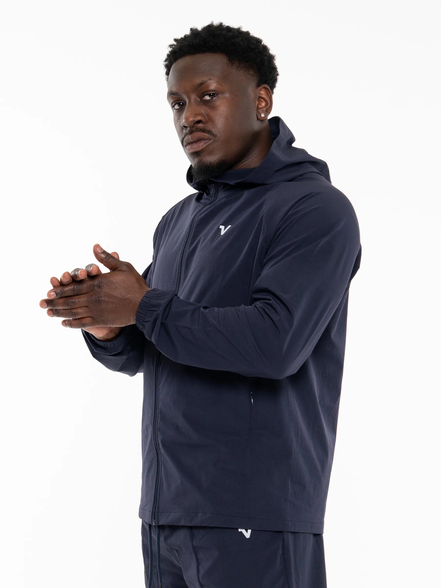 Veritone Mode Jacket, Deep Navy – A man wearing a navy blue hooded athletic jacket and matching pants, posed against a clean white studio background.