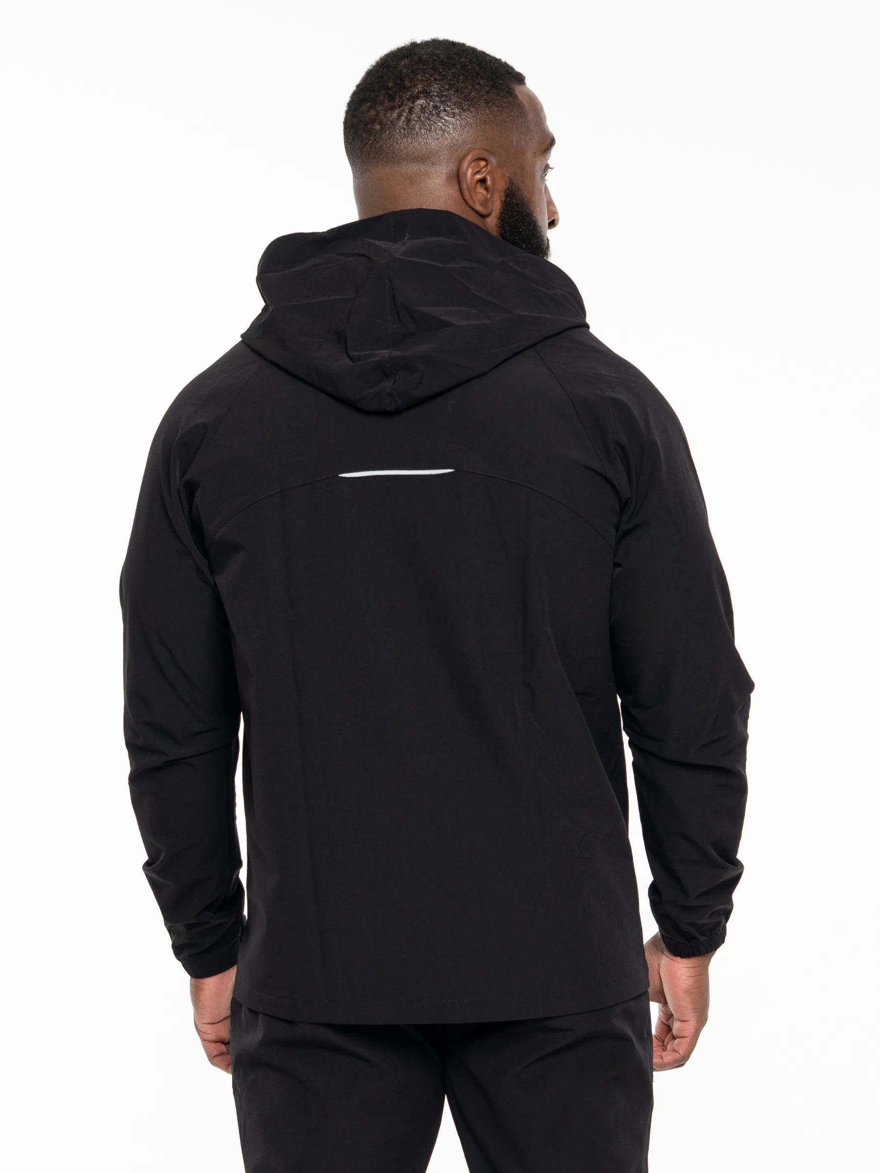 Veritone Mode Jacket, Midnight Black – A man viewed from the back wearing a black hooded jacket with a small horizontal reflective stripe on the upper back, set against a plain white studio background.