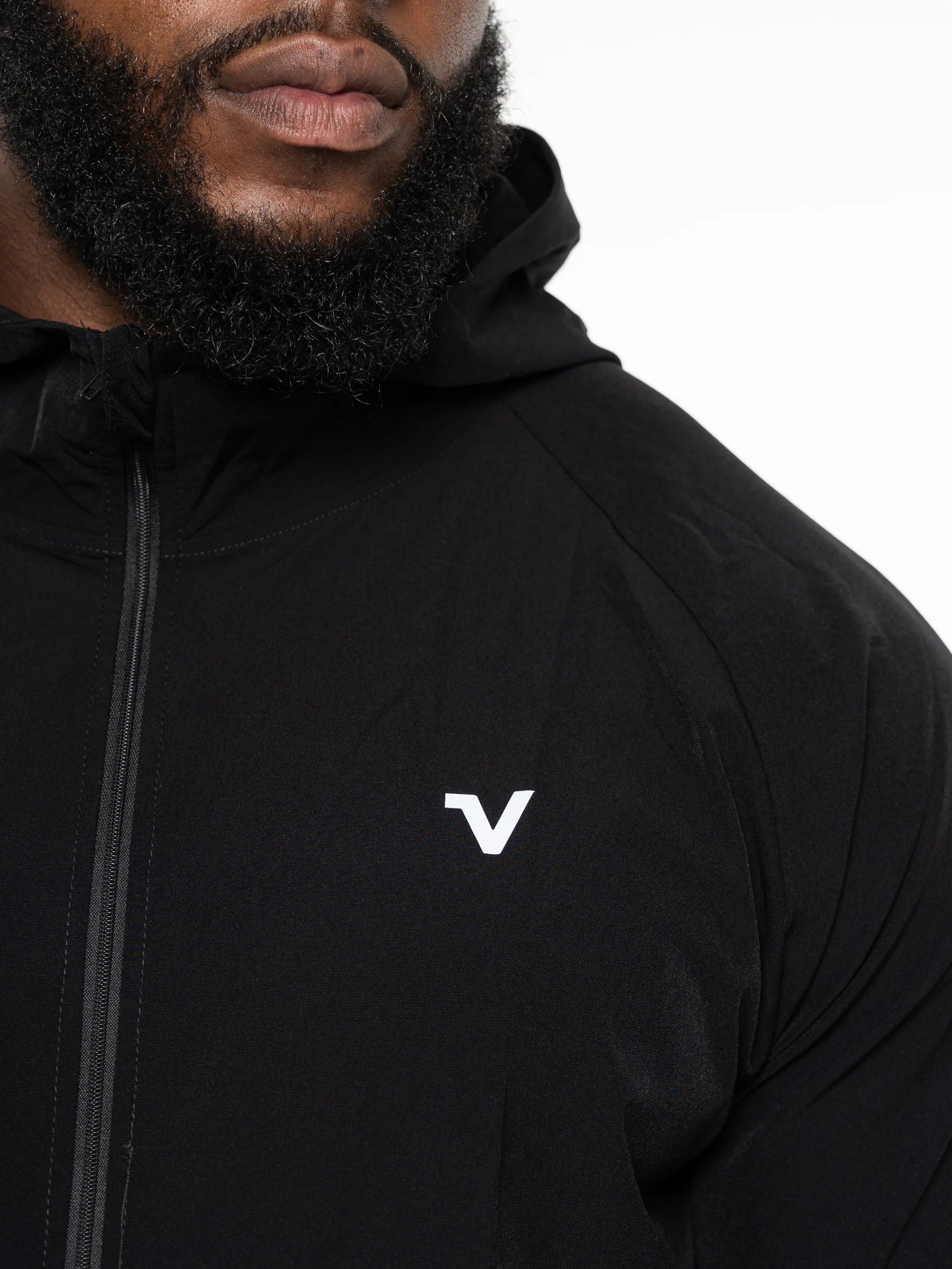 Veritone Mode Jacket, Midnight Black – Close-up of a man wearing a black hooded jacket with a white stylized 'V' logo on the left chest, against a plain white background.