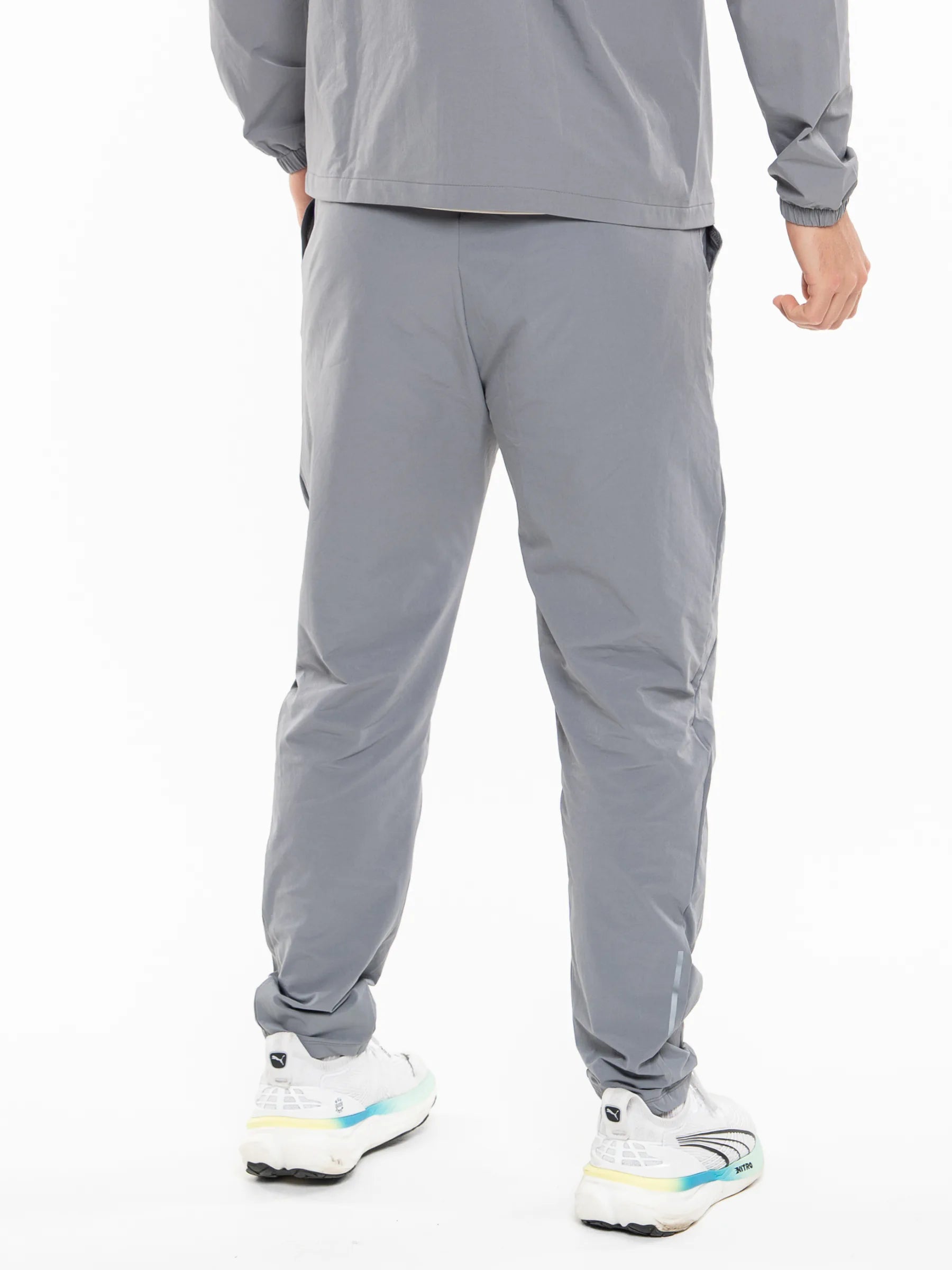 Veritone Mode Track Pants, Ash Grey – A person shown from the back wearing light gray athletic jogger pants, a matching gray long-sleeve top, and white running shoes with light blue and yellow accents, against a plain white studio background.