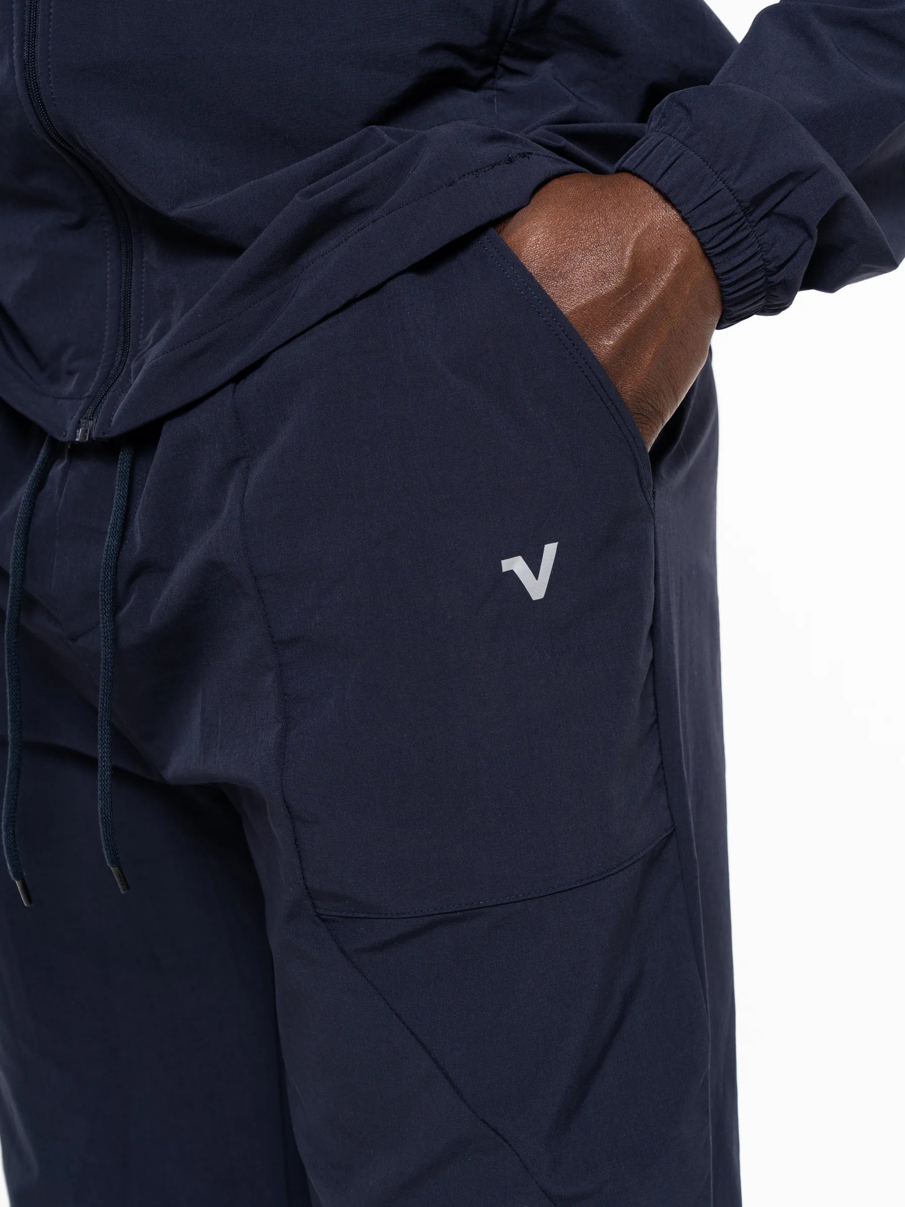 Veritone Mode Track Pants, Deep Navy – Close-up of a person wearing dark navy pants with a side pocket and a small white stylized 'V' logo on the pocket, with a hand in the pocket.