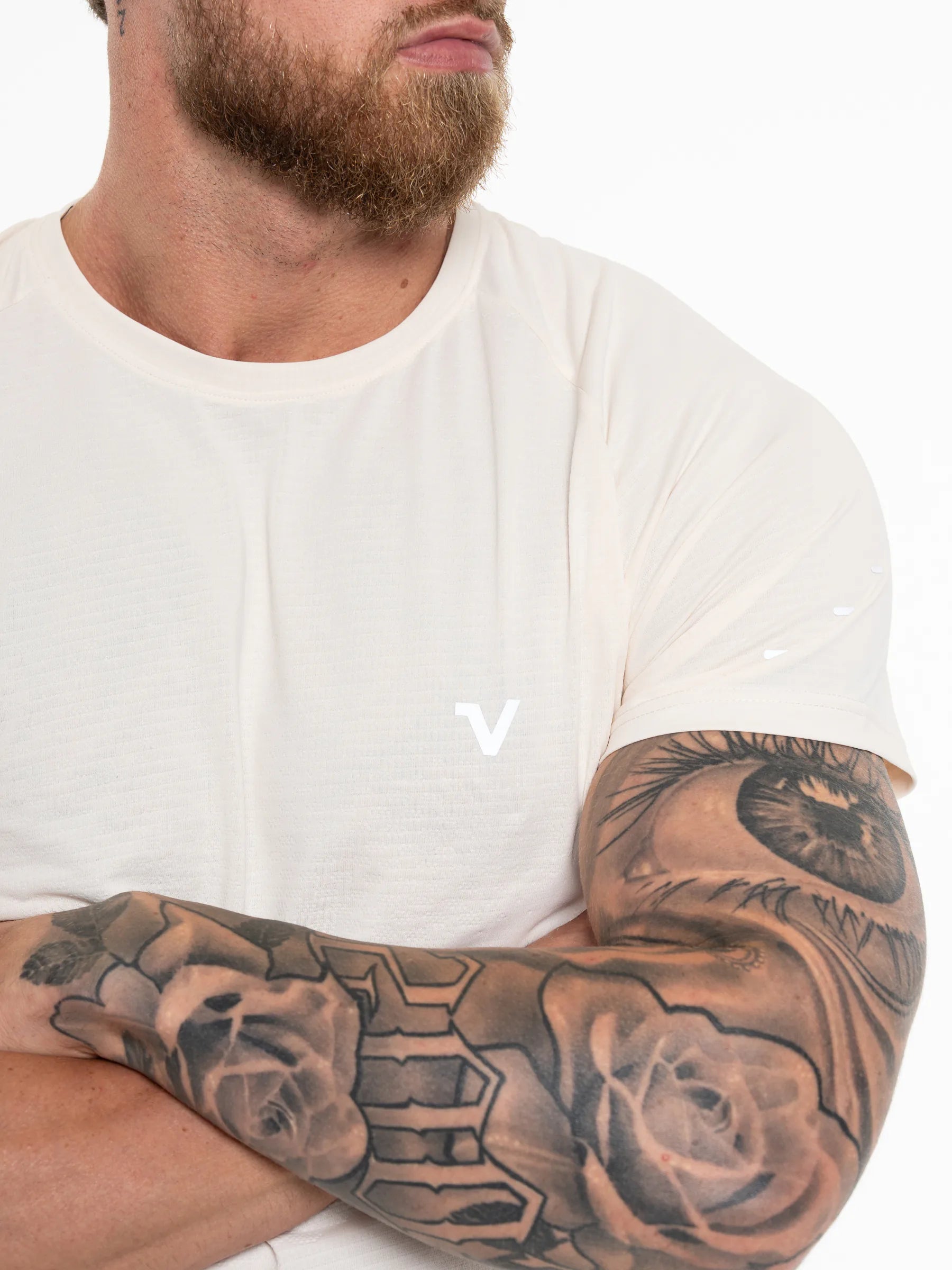 Veritone Prime Core T-Shirt, Cloud Cream – A close-up of a man's tattooed arm and lower face wearing a white crew-neck t-shirt with a small white stylized 'V' logo on the chest, set against a plain white background.