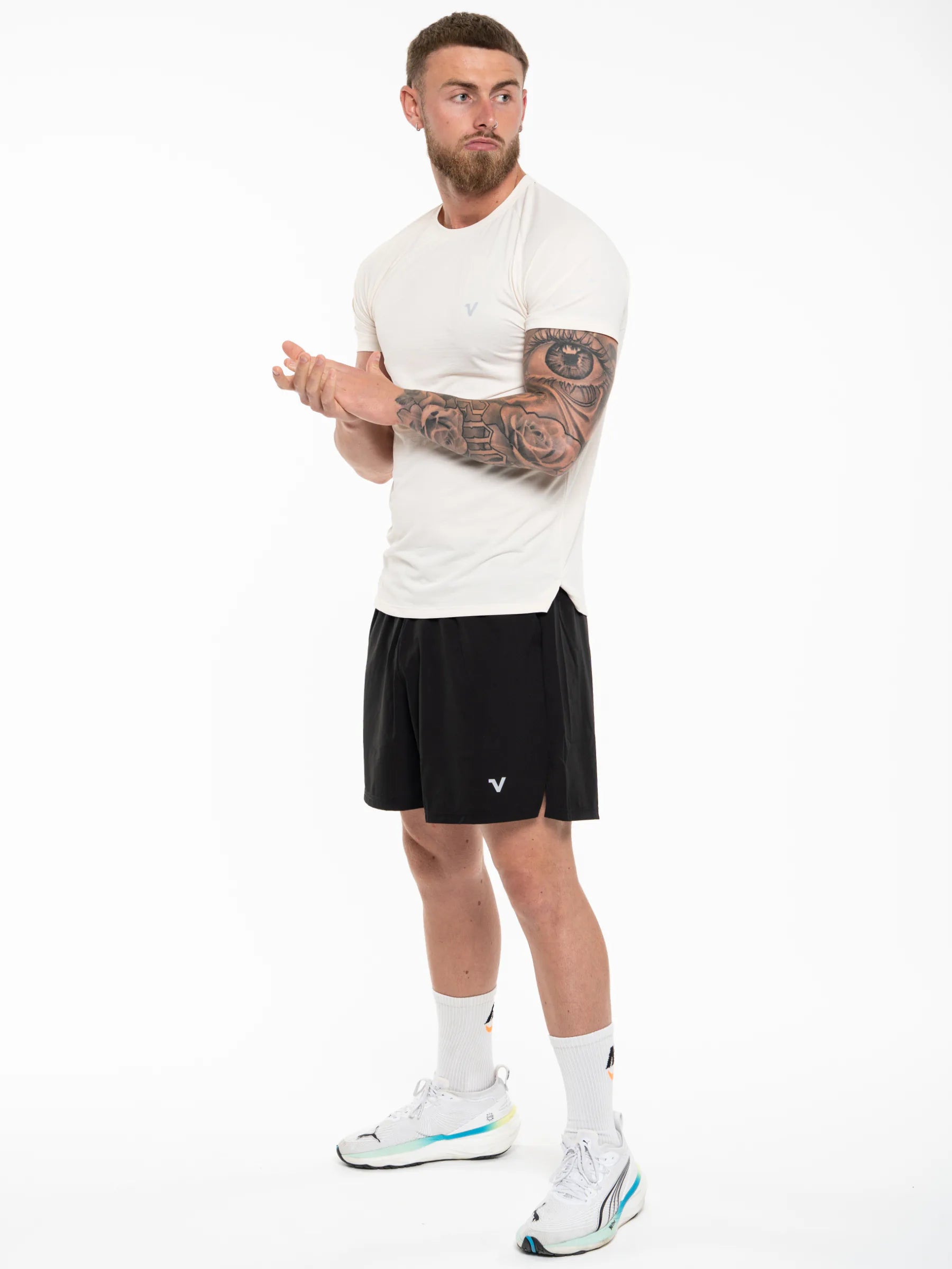 Veritone Prime Core T-Shirt, Cloud Cream – A man modeling athletic wear, featuring a white short-sleeve athletic t-shirt and black athletic shorts with a small white logo, paired with white socks and white running shoes.