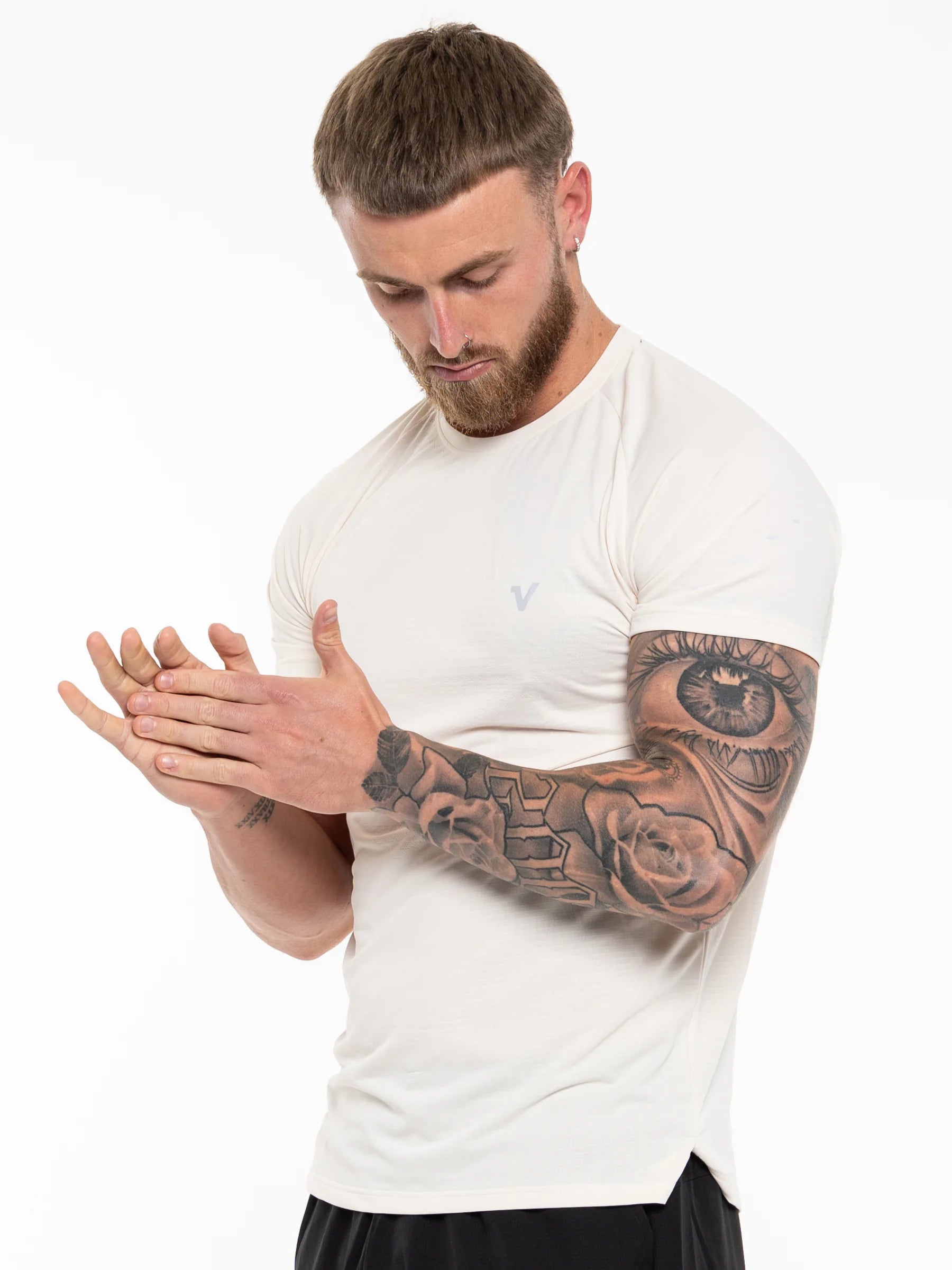 Veritone Prime Core T-Shirt, Cloud Cream – A man with a beard and extensive arm tattoos wearing a fitted white athletic t-shirt, shown from the waist up against a plain white background.