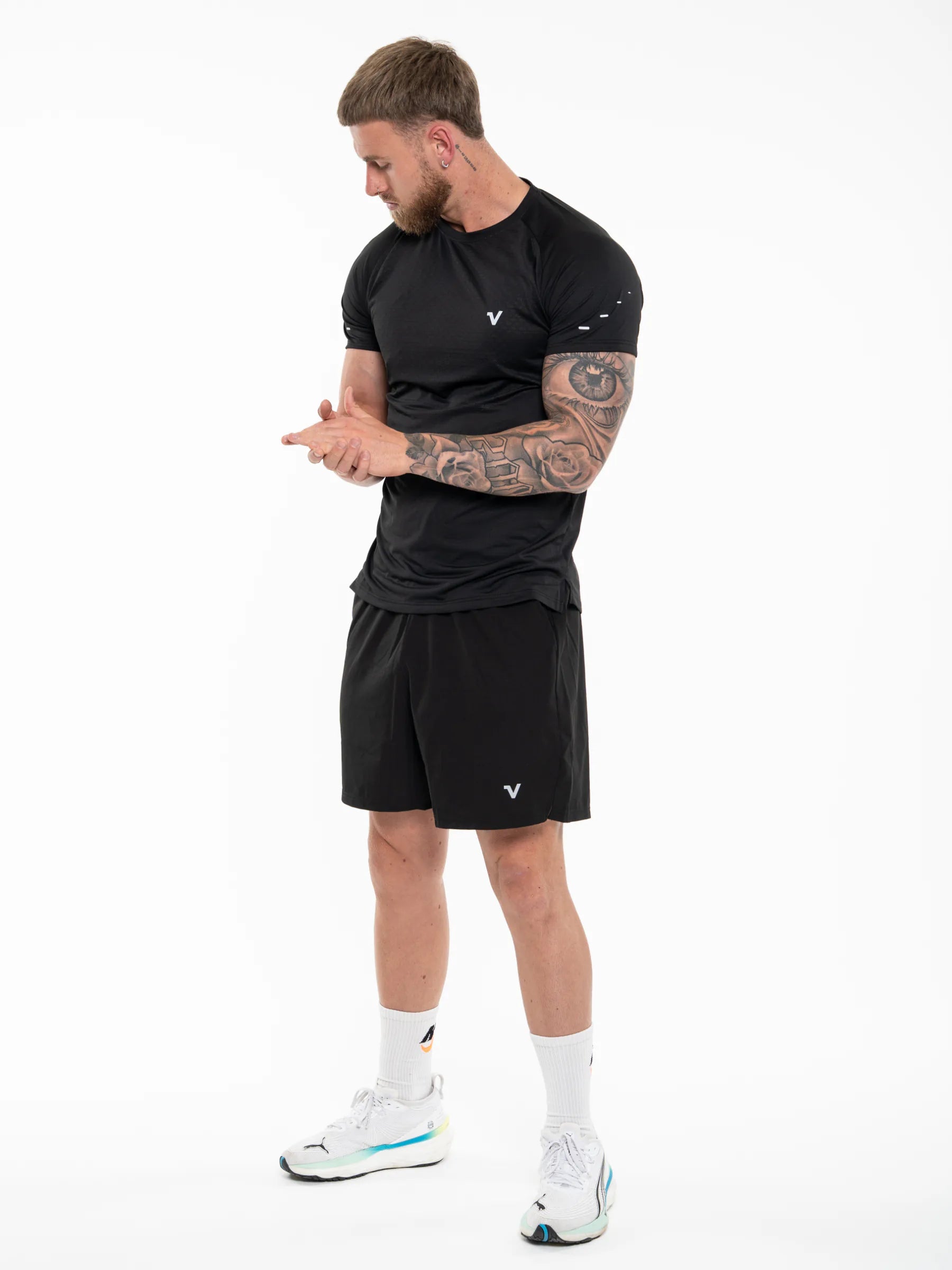 Veritone Prime Core T-Shirt, Midnight Black – A man modeling a black athletic t-shirt and matching black shorts with a small white logo, paired with white socks and white sneakers, against a plain white studio background.