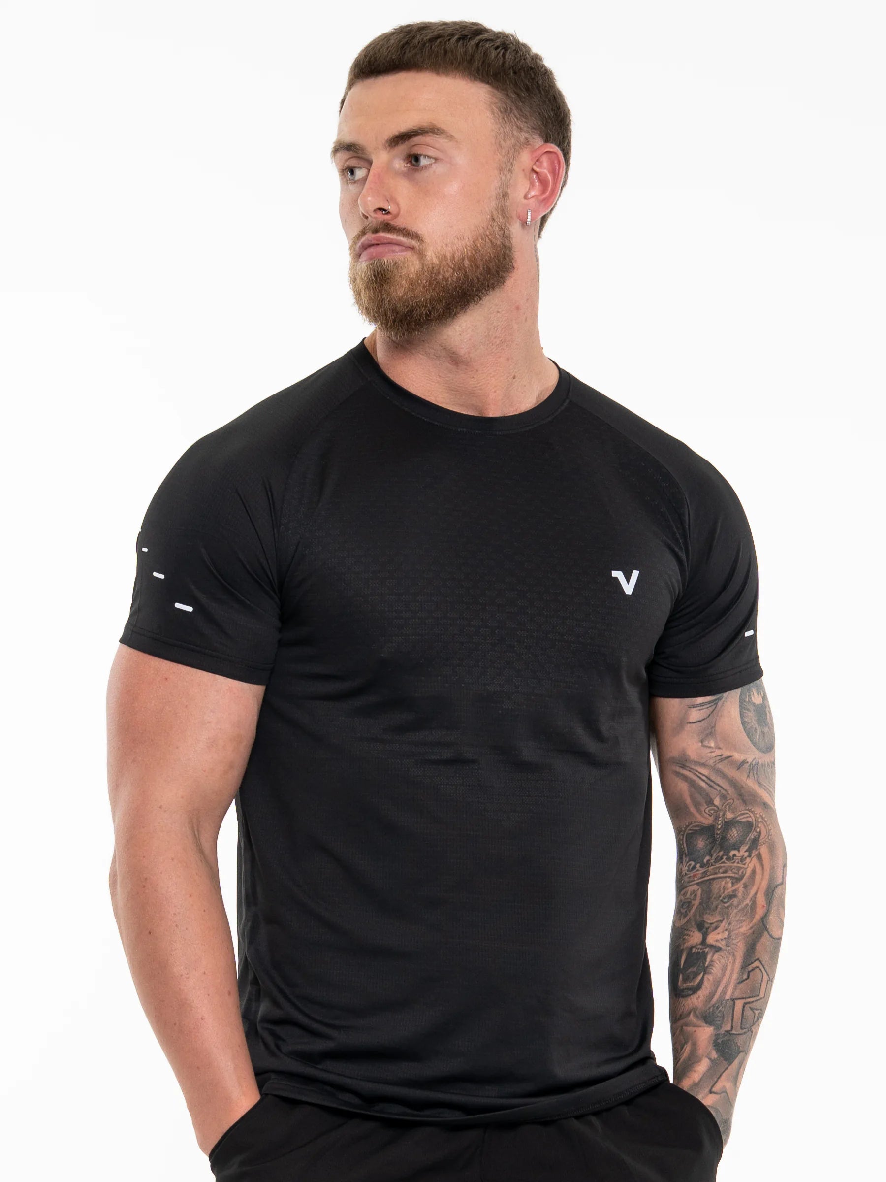 Veritone Prime Core T-Shirt, Midnight Black – A muscular man with a beard and arm tattoos wearing a black short-sleeve athletic t-shirt with a small white logo on the left chest, photographed against a solid white background.