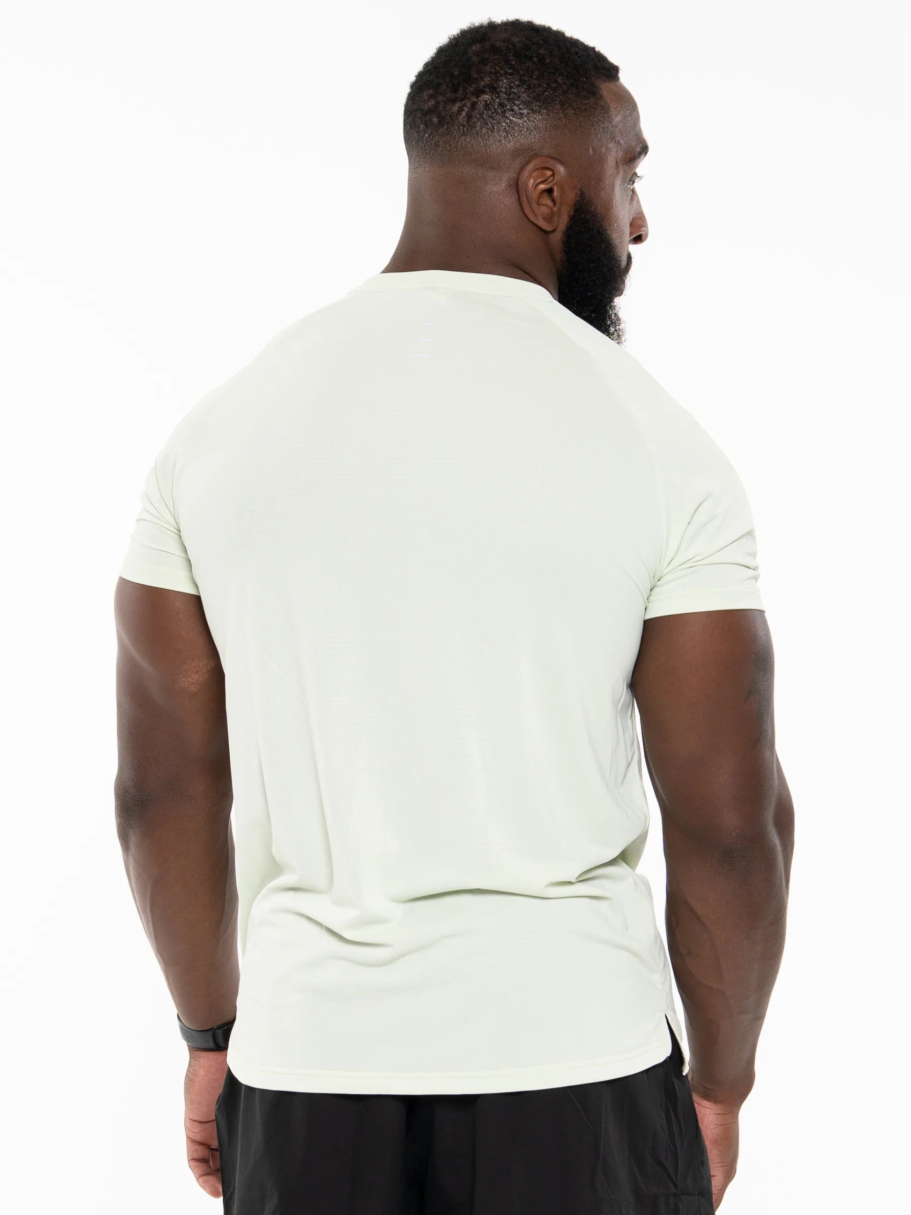 Veritone Prime Core T-Shirt, Volt Green – A man viewed from behind wearing a pale sage green athletic t-shirt and black shorts against a white studio background.