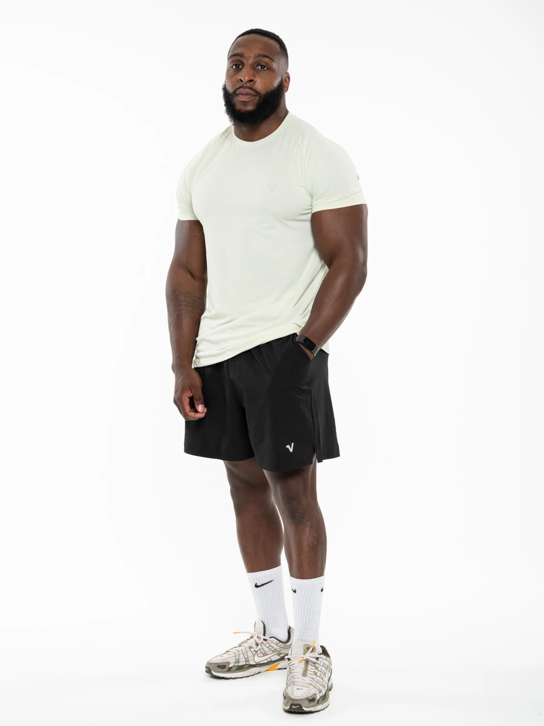 Veritone Prime Core T-Shirt, Volt Green – A man modeling athletic wear consisting of a light cream t-shirt, black athletic shorts, white socks, and athletic shoes, standing against a solid white background.