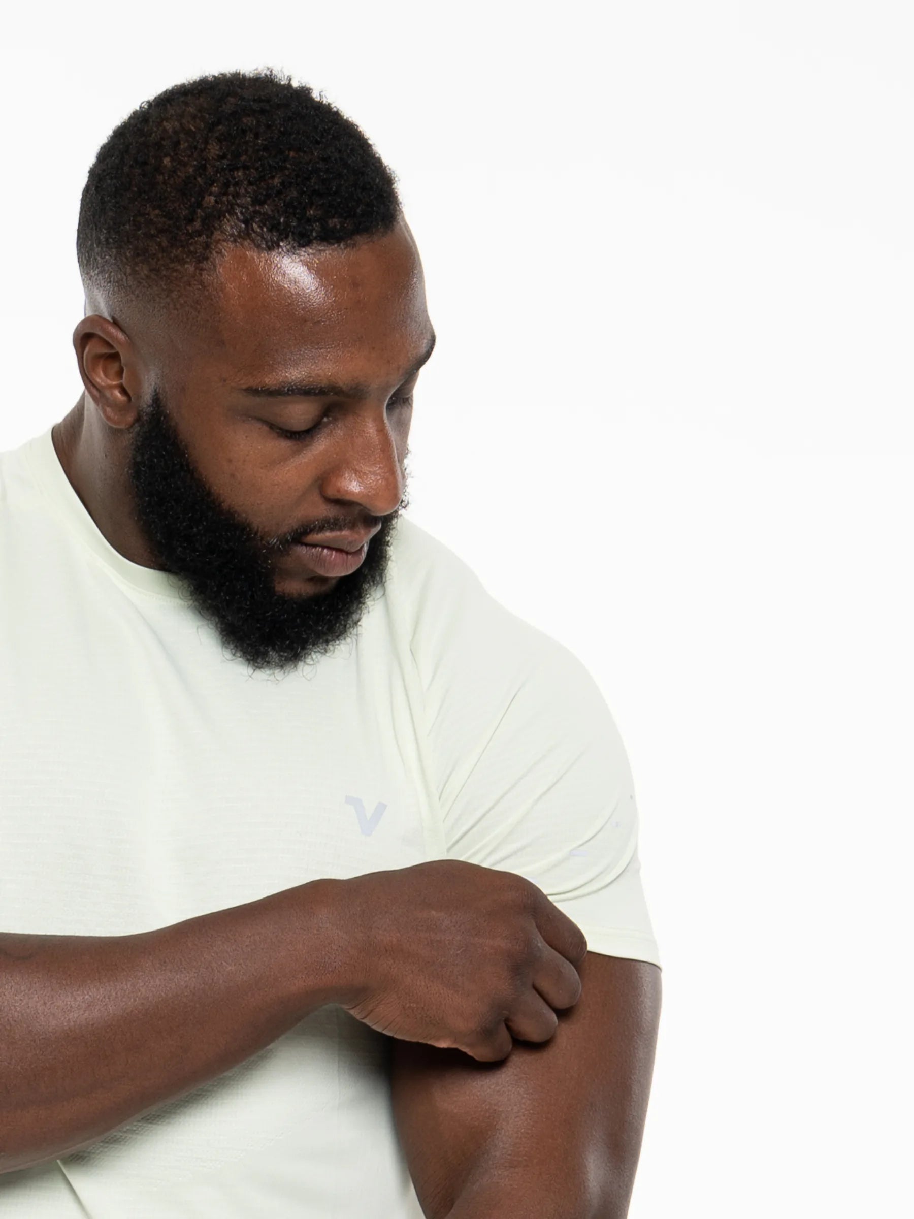 Veritone Prime Core T-Shirt, Volt Green – A man with a beard wearing a pale green t-shirt, looking down and adjusting his sleeve, against a plain white background.