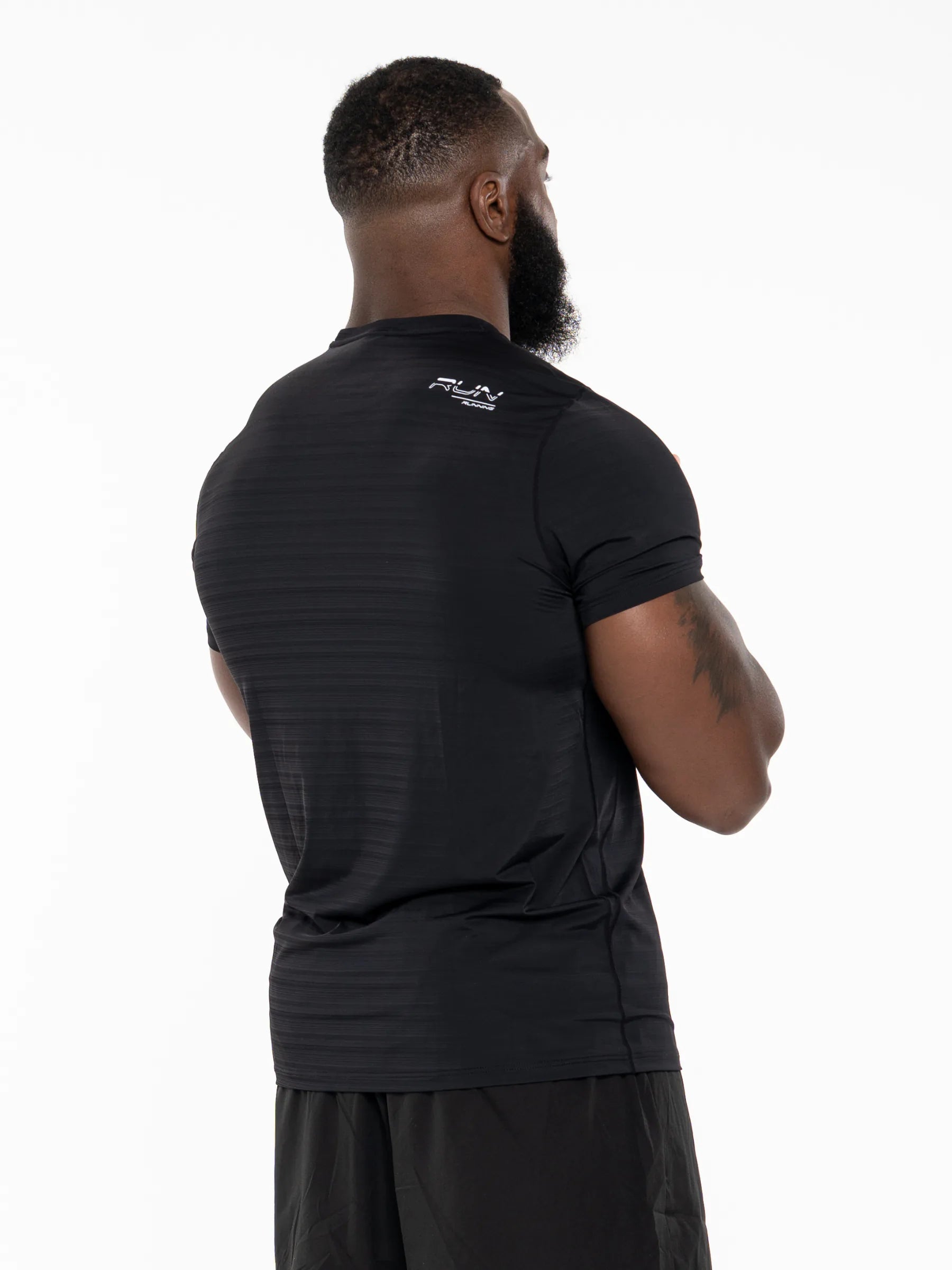 Veritone Prime Muscle Fit T-Shirt, Black – A man viewed from the back wearing a black short-sleeve athletic compression shirt with a small white logo on the upper back, paired with black shorts, against a plain white studio background.