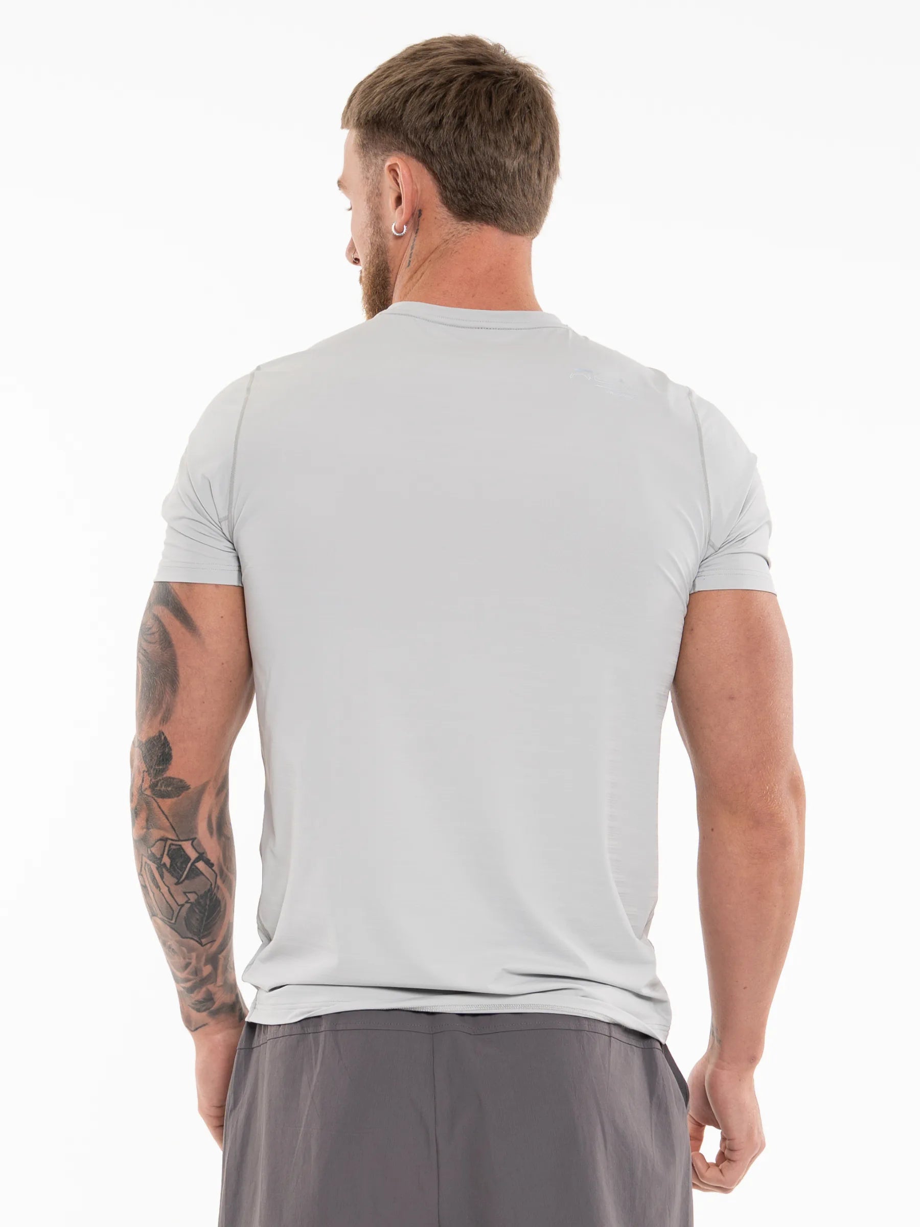 Veritone Prime Muscle Fit T-Shirt, Light Grey – A man viewed from behind wearing a light gray short-sleeve athletic t-shirt and dark gray shorts against a plain white background.