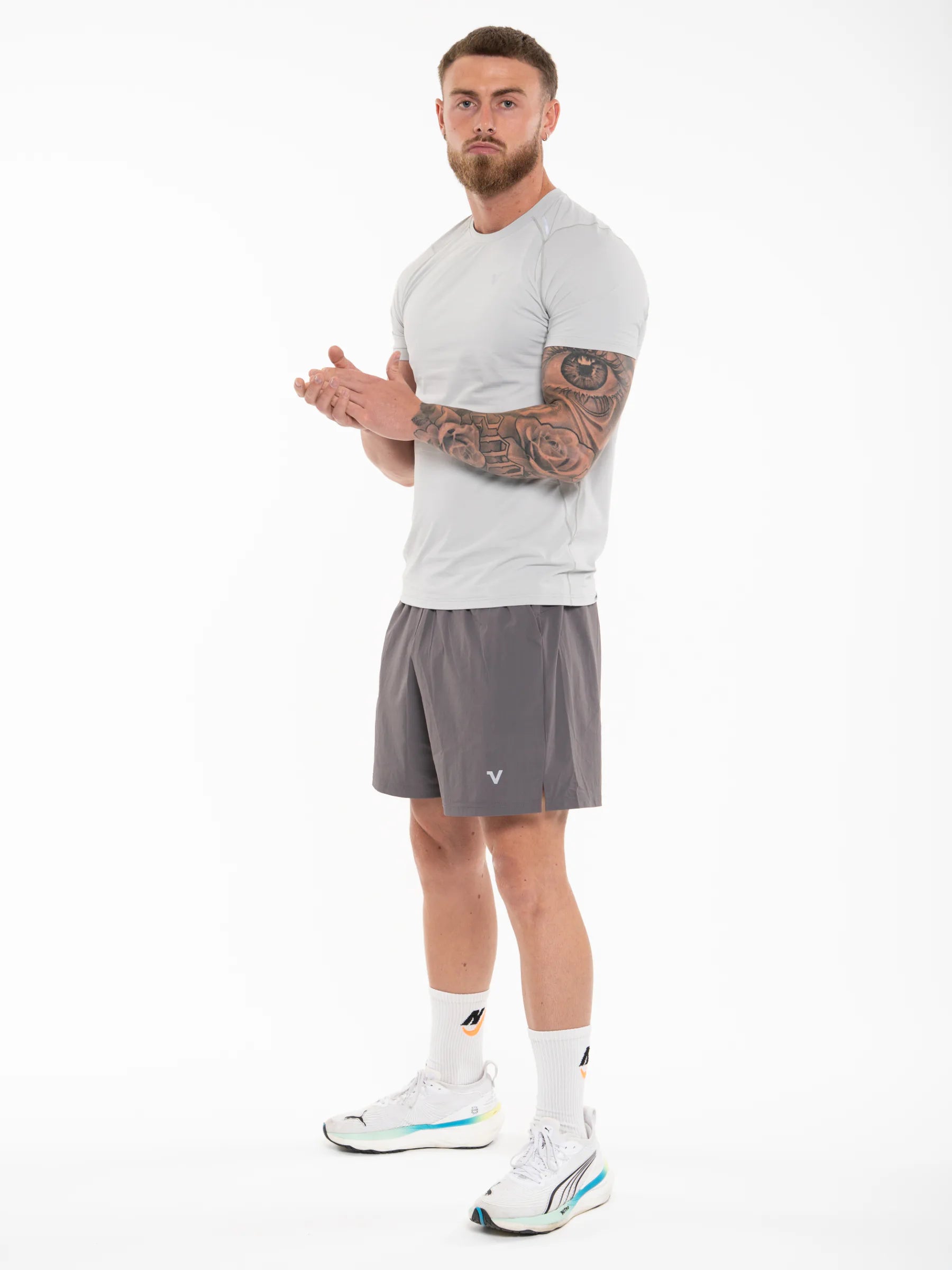 Veritone Prime Muscle Fit T-Shirt, Light Grey – A man modeling athletic wear, featuring a light gray short-sleeve athletic t-shirt and dark gray athletic shorts, paired with white socks and white running shoes, against a plain white studio background.