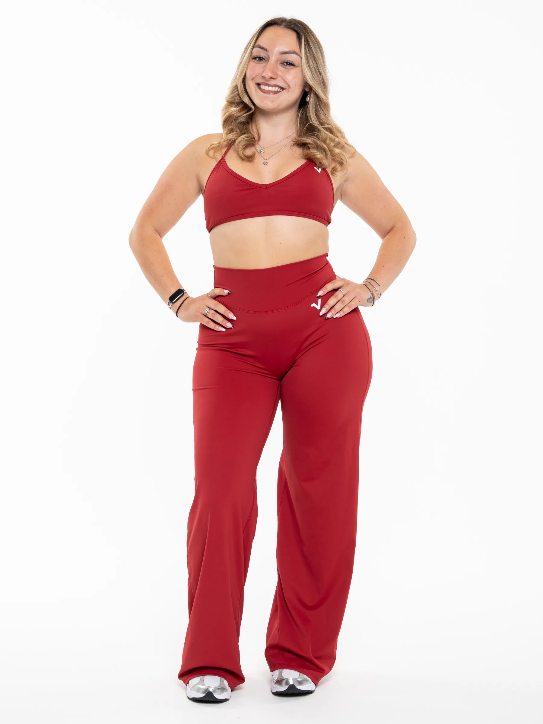 Veritone Sculpt Flared Pants, Crimson Red – A woman modeling a matching red activewear set consisting of a sports bra and high-waisted wide-leg pants, standing against a solid white background.