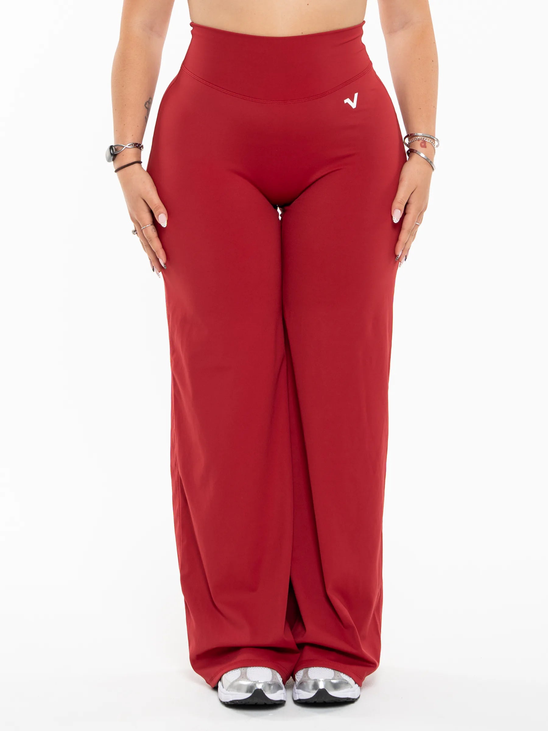 Veritone Sculpt Flared Pants, Crimson Red – A model wearing high-waisted, wide-leg red pants with a small white logo on the upper right hip, paired with silver shoes, against a plain white background.