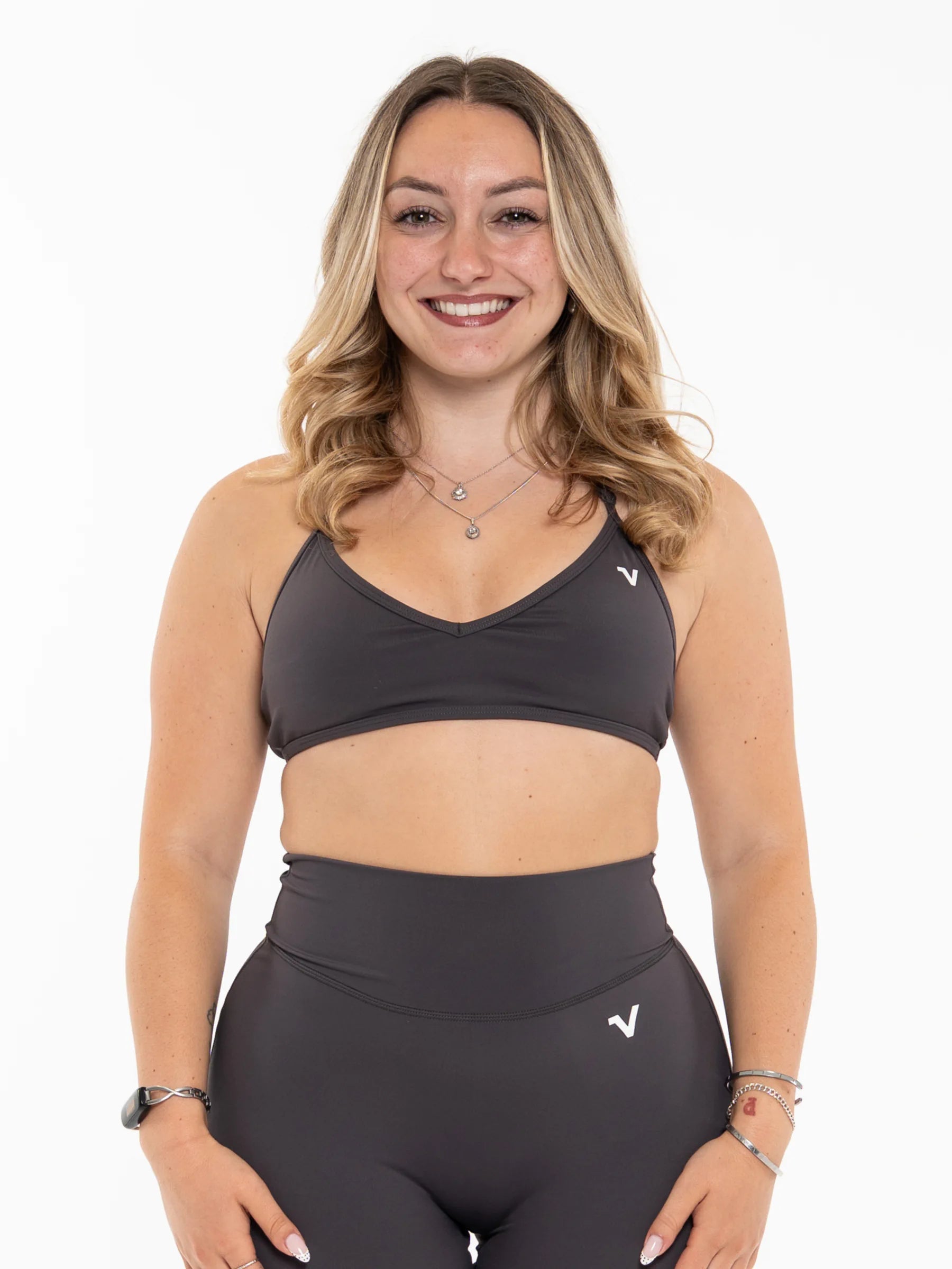 Veritone Sculpt Sports Bra, Charcoal Grey – A smiling blonde woman wearing a matching dark gray athletic set consisting of a sports bra and high-waisted leggings, photographed against a solid white background.