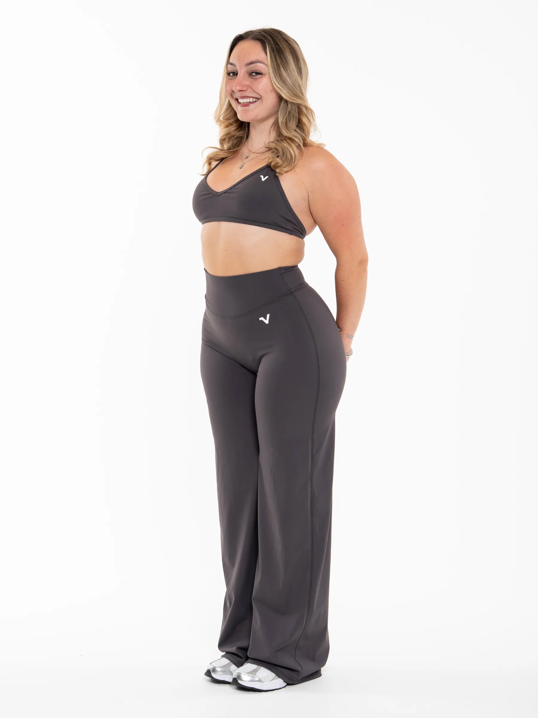 Veritone Sculpt Sports Bra, Charcoal Grey – A woman modeling a dark gray athletic set consisting of a sports bra and high-waisted wide-leg pants, shown from a side profile against a plain white studio background.