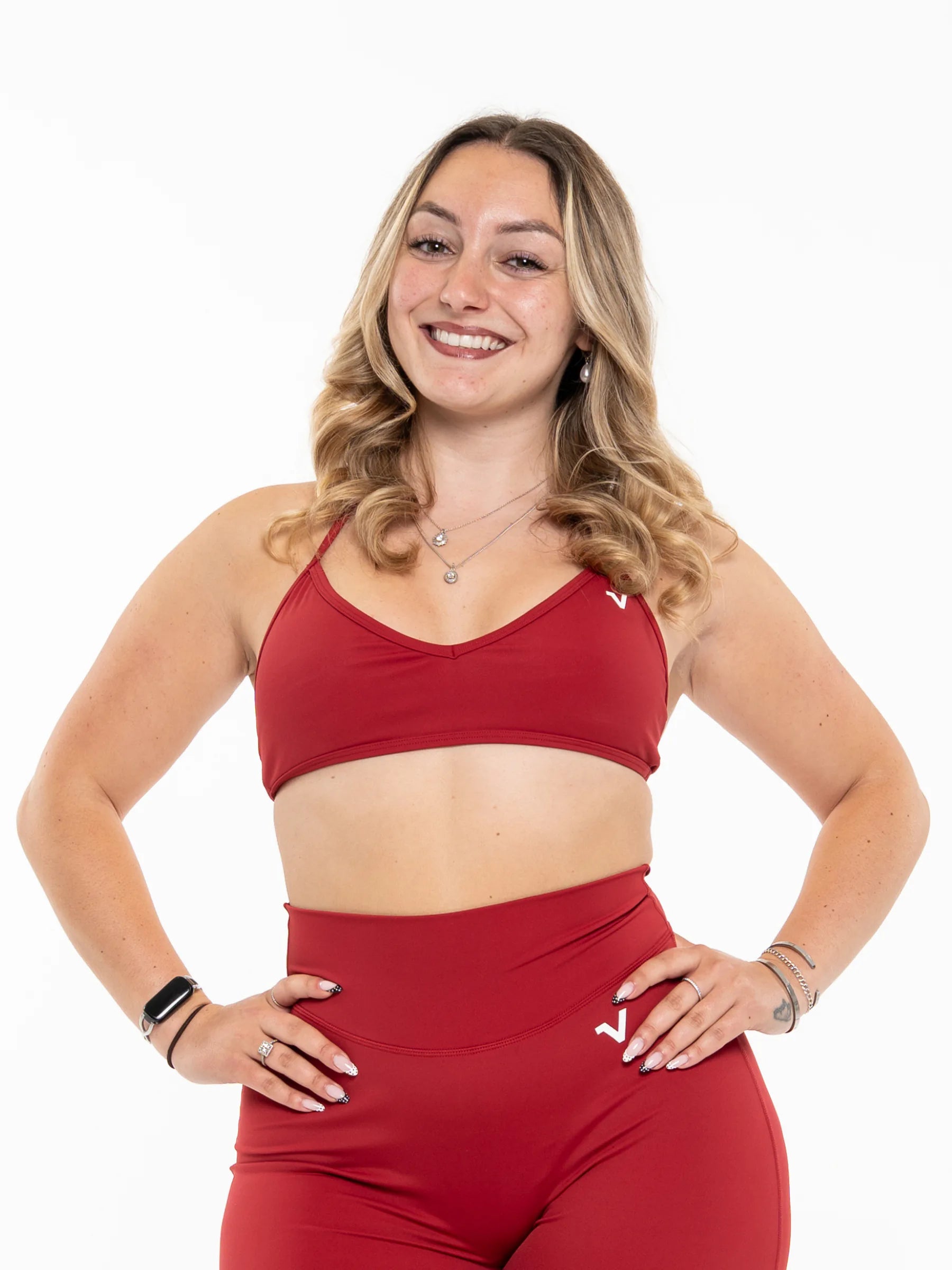 Veritone Sculpt Sports Bra, Crimson Red – A woman modeling a matching red activewear set consisting of a sports bra and high-waisted leggings, posed against a solid white background.