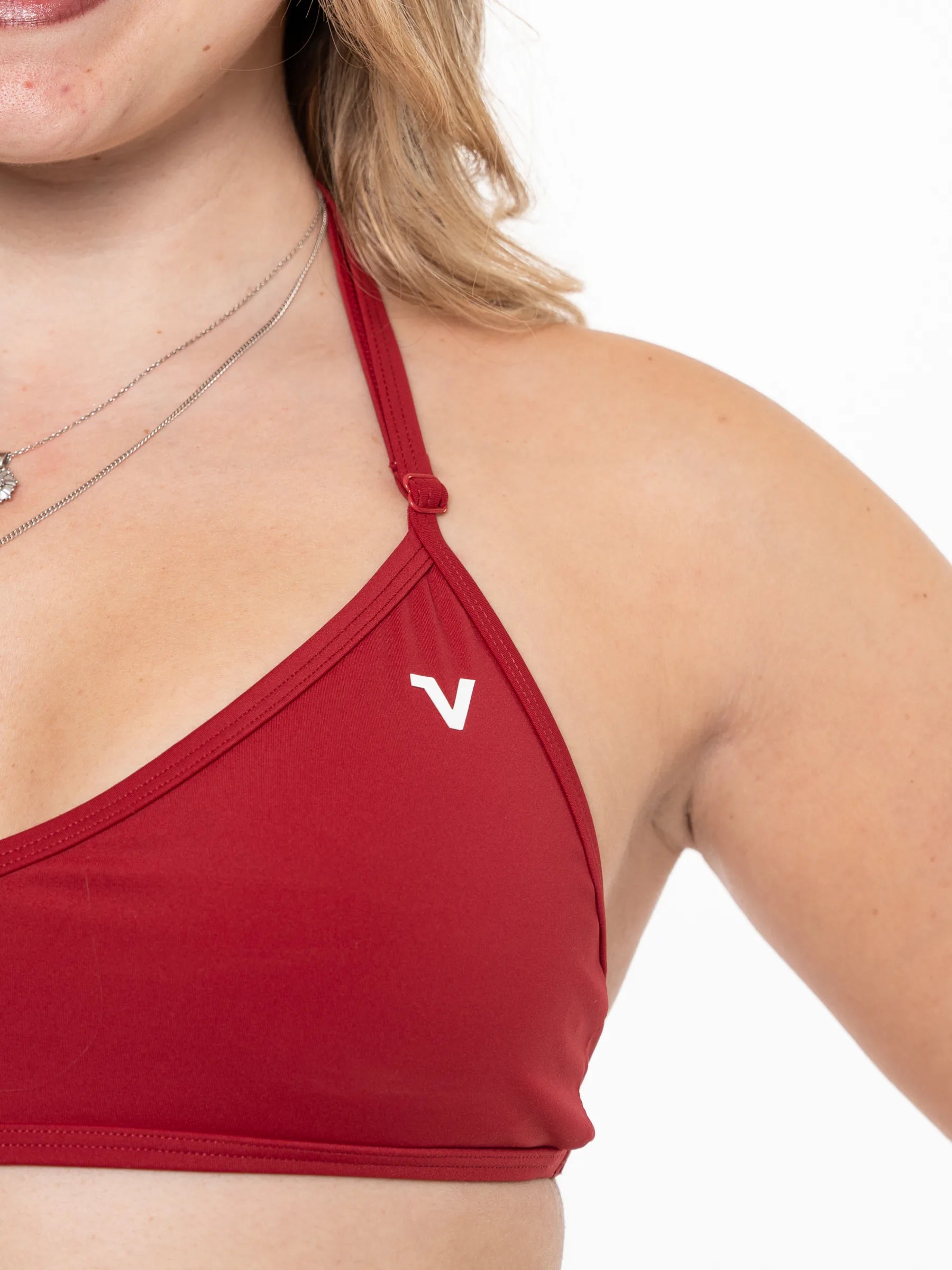 Veritone Sculpt Sports Bra, Crimson Red – Close-up of a woman wearing a red sports bra with a small white stylized 'V' logo on the left cup, photographed against a plain white background.