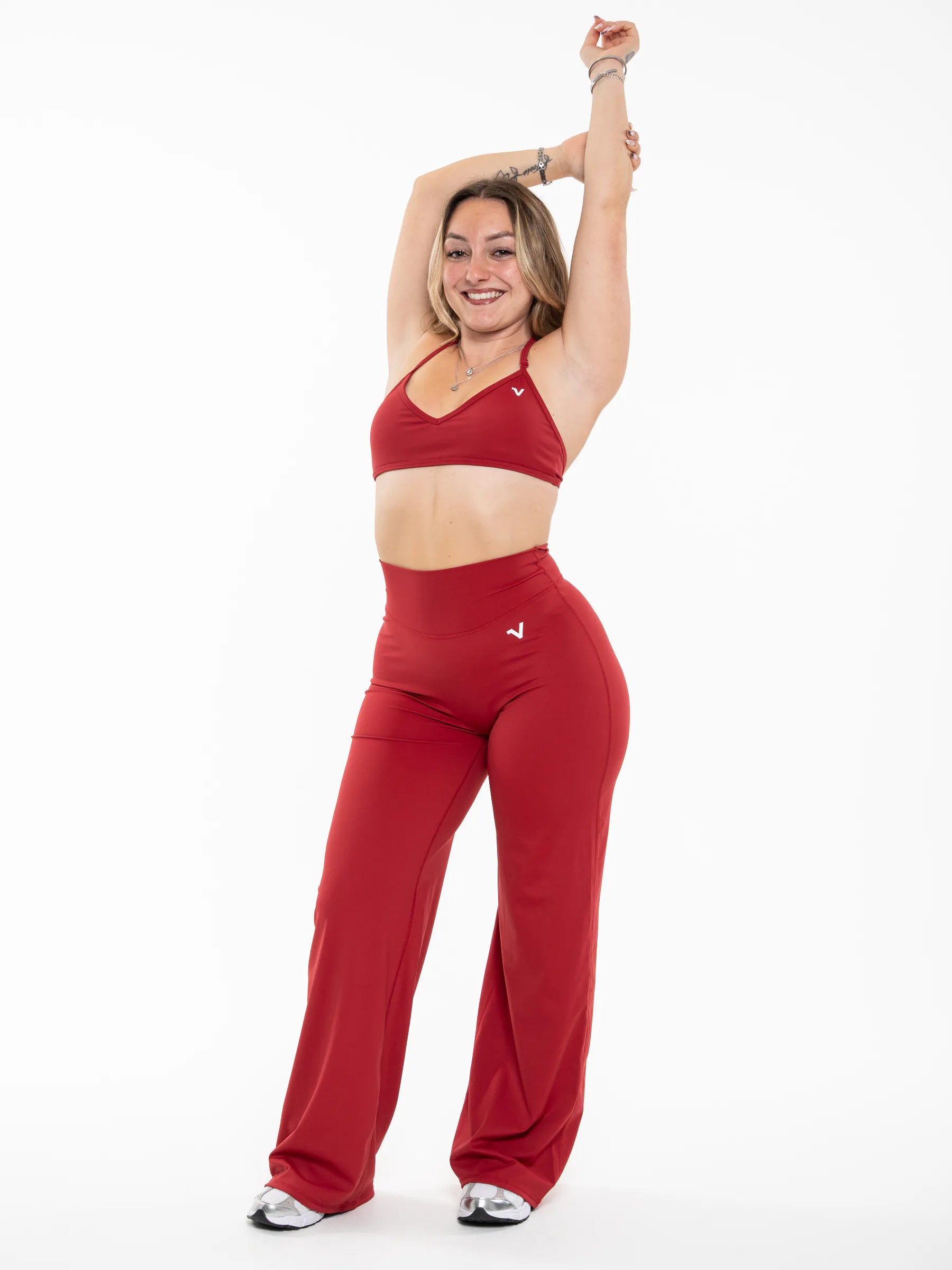 Veritone Sculpt Sports Bra, Crimson Red – A woman modeling a matching red activewear set consisting of a sports bra and high-waisted wide-leg pants, posing against a solid white background.